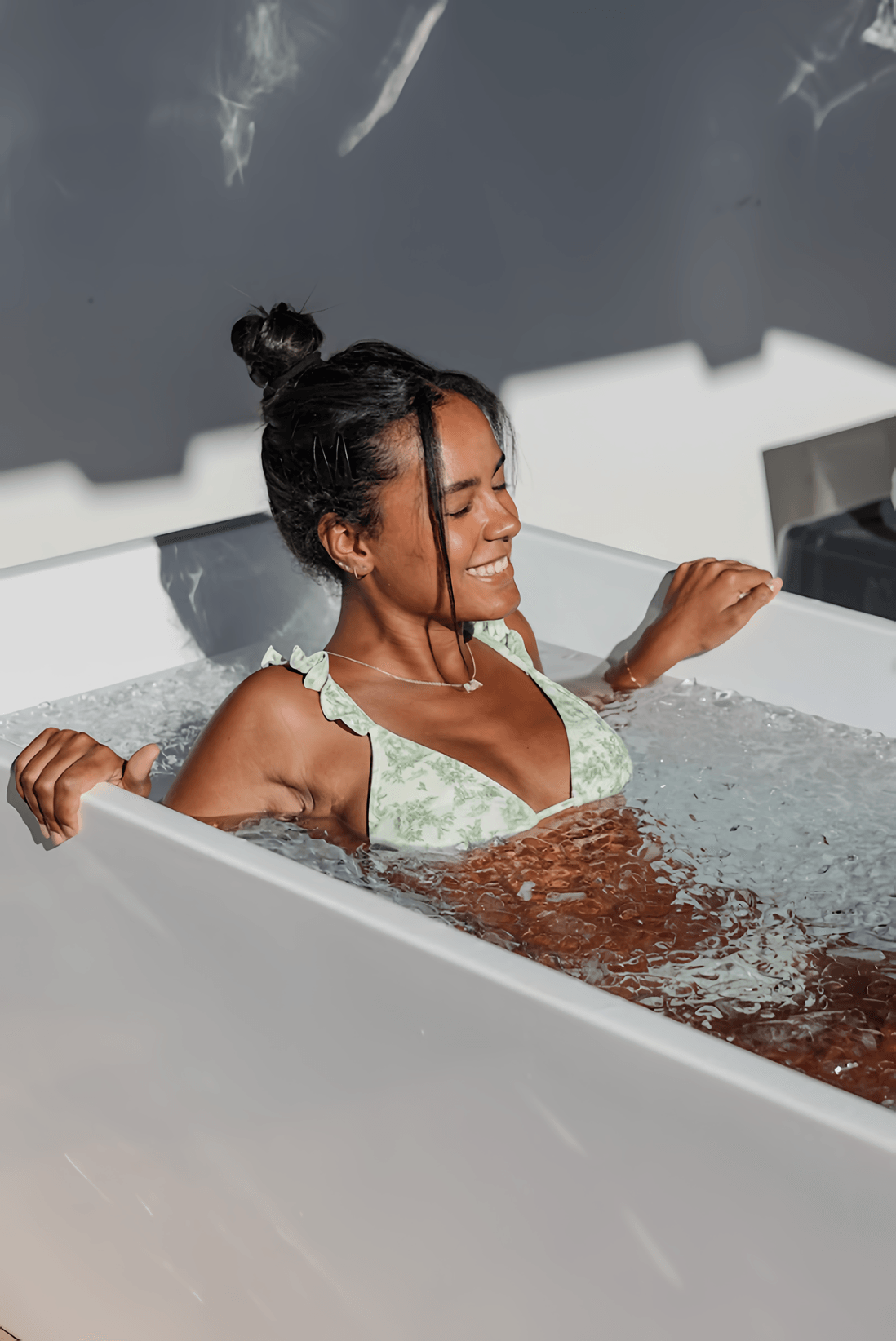 Smiling woman in a patterned swimsuit sitting in a bathtub.