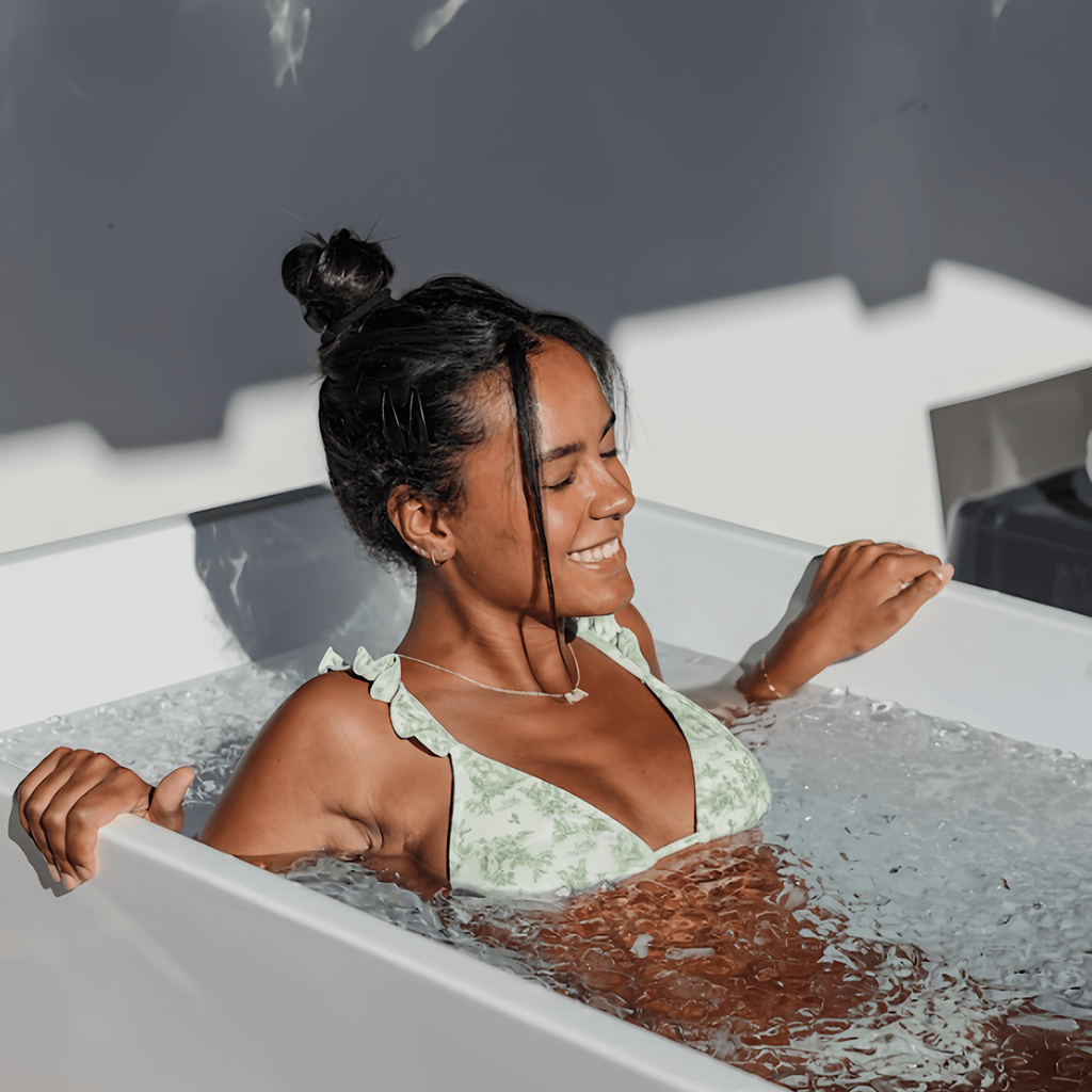 Smiling woman in a patterned swimsuit sitting in a bathtub.