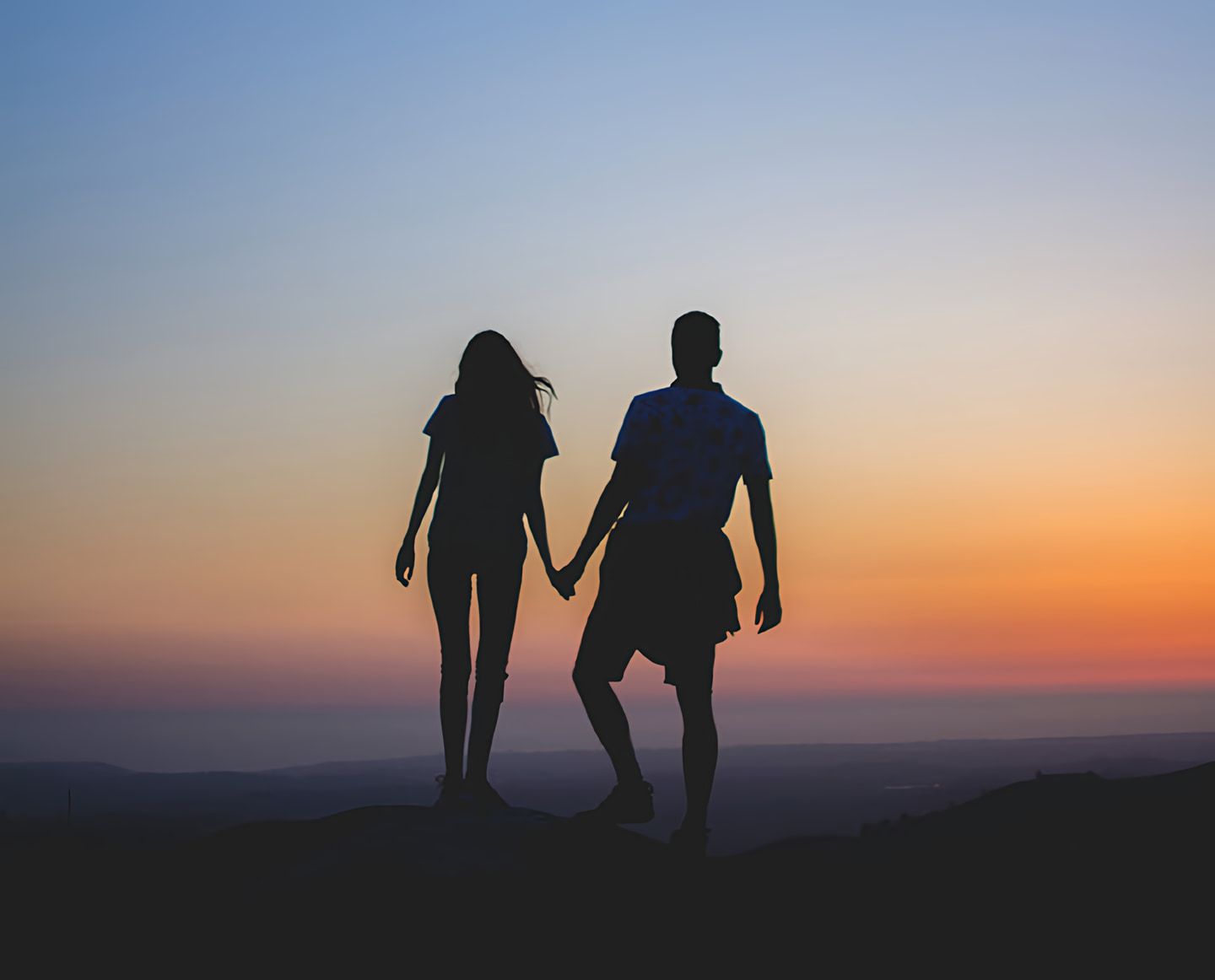 Silhouetted couple holding hands on a hill at sunset.
