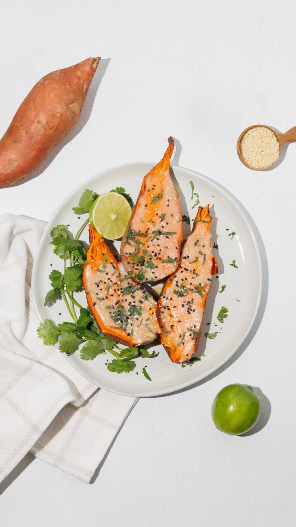 Roasted sweet potato wedges with a pale sauce, cilantro, lime, and sesame seeds on a white plate.