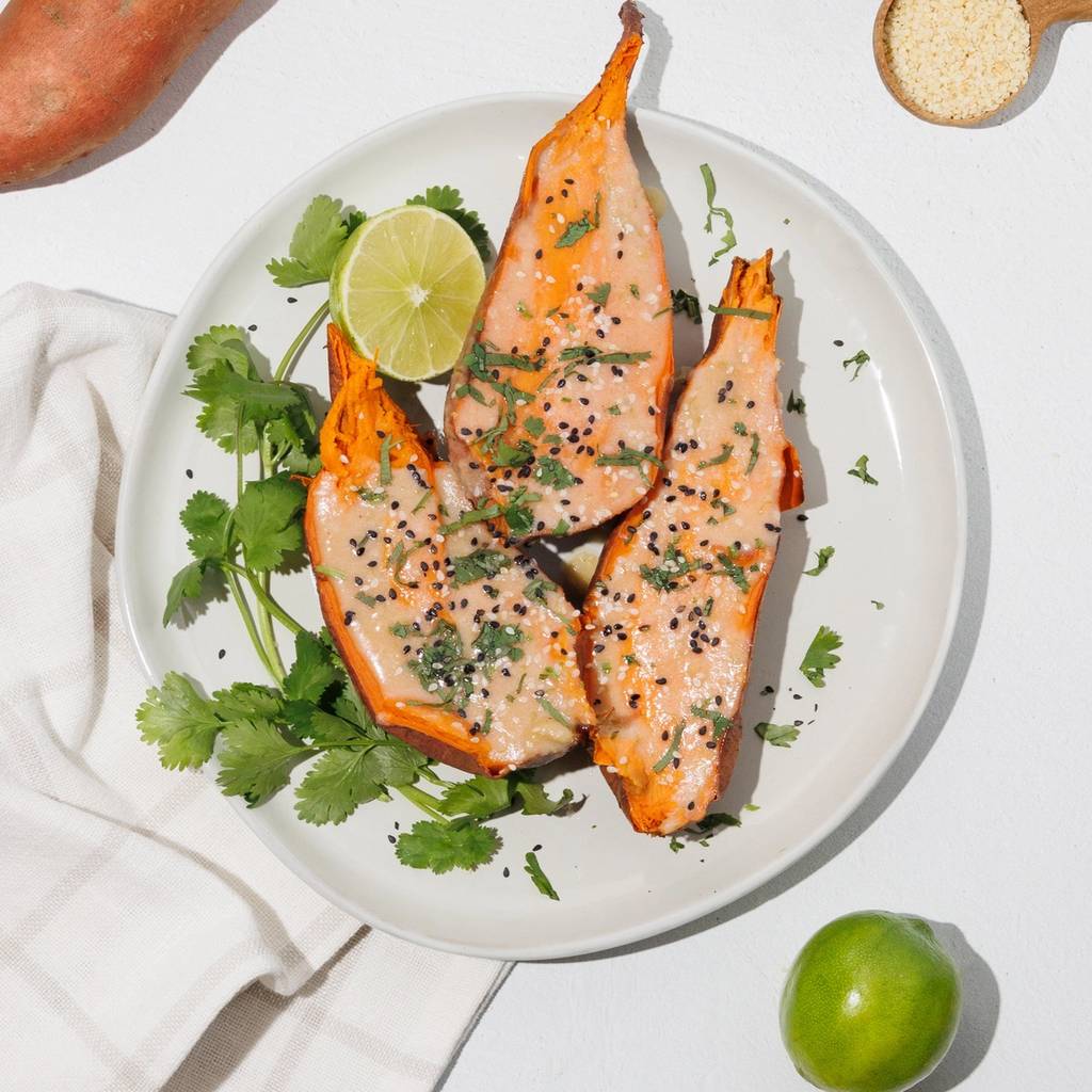 Roasted sweet potato wedges with a pale sauce, cilantro, lime, and sesame seeds on a white plate.