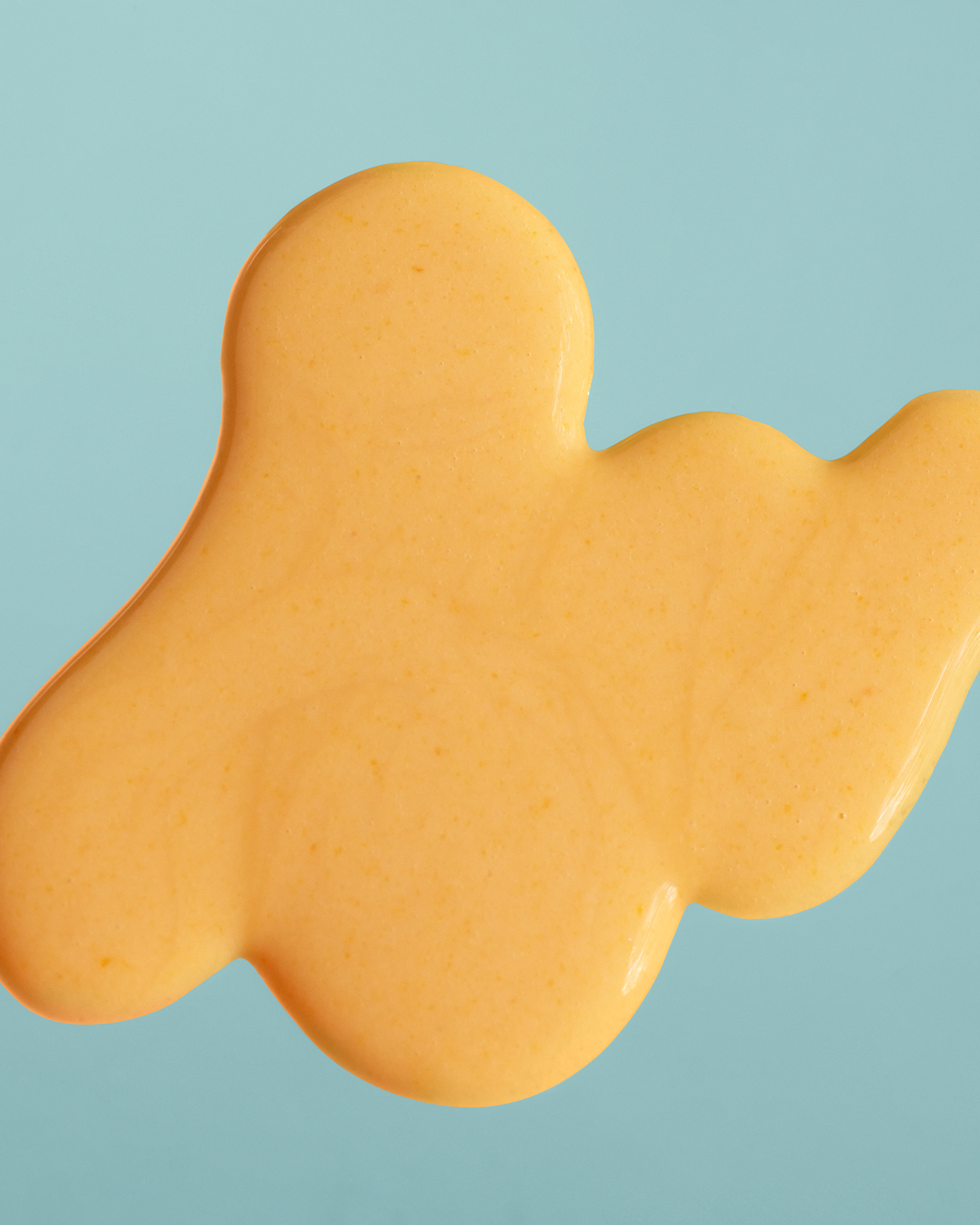 Close-up of a glossy golden-orange smear against a pale blue background.