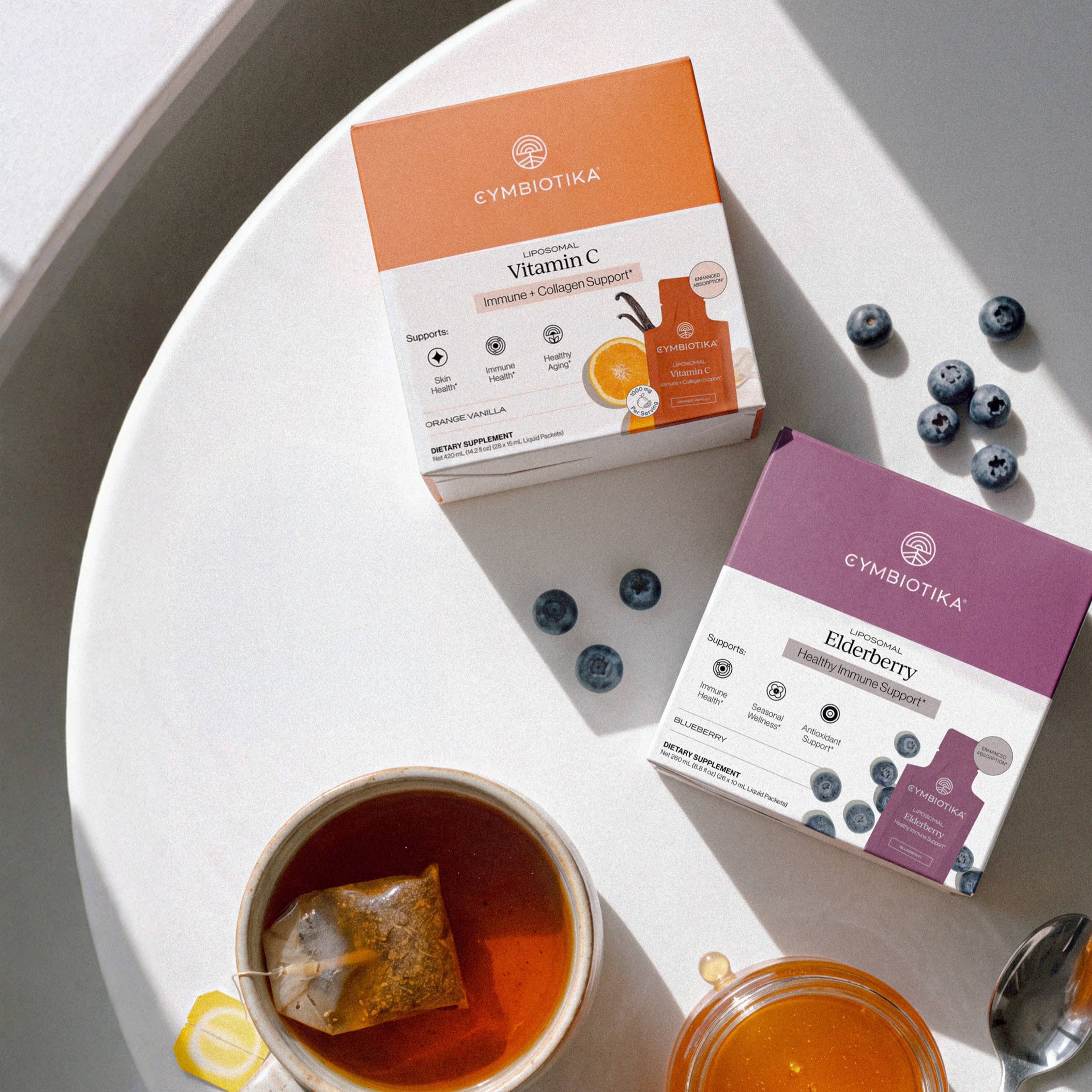 Liposomal Vitamin C and Liposomal Elderberry packages beside blueberries and a cup of tea.