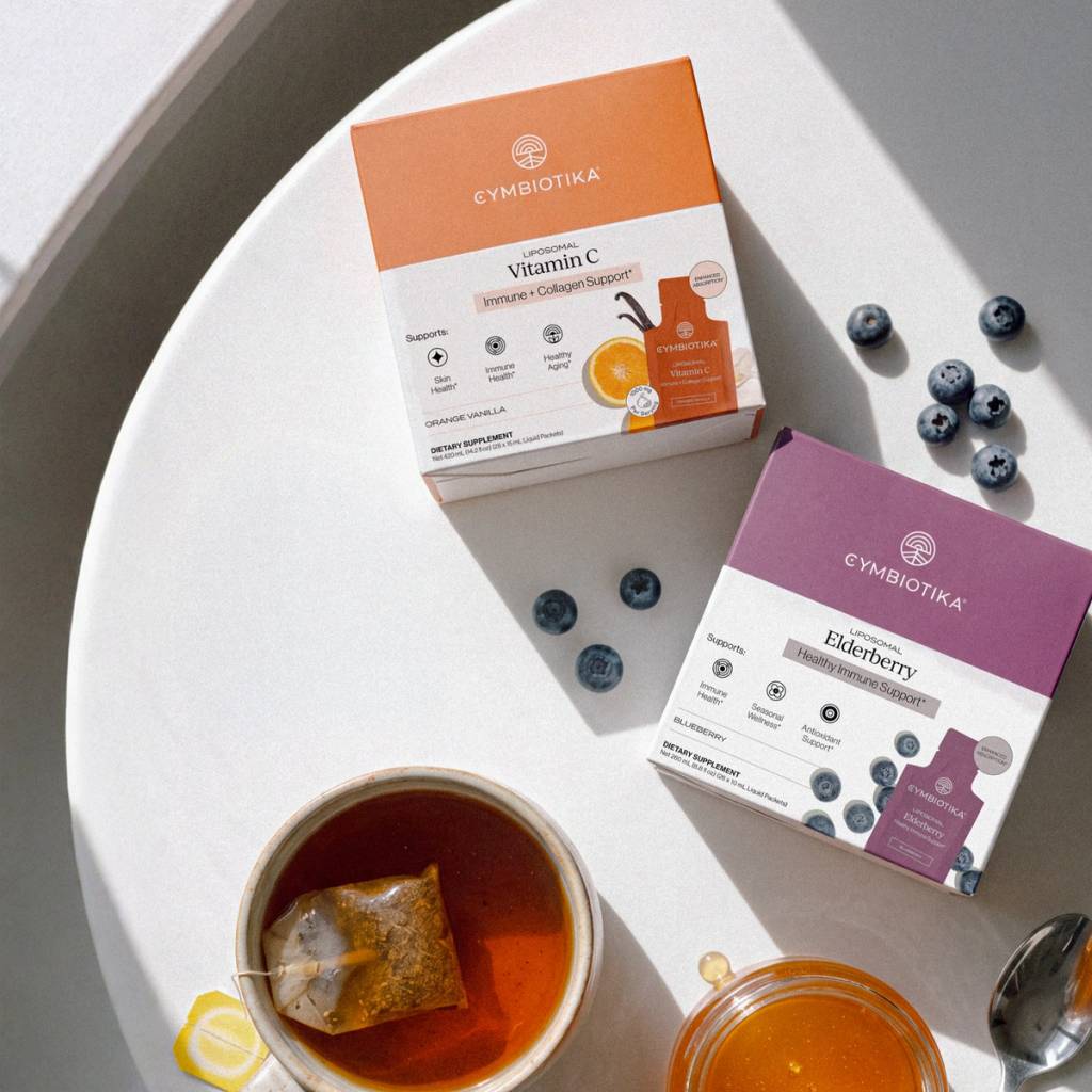 Liposomal Vitamin C and Liposomal Elderberry packages beside blueberries and a cup of tea.