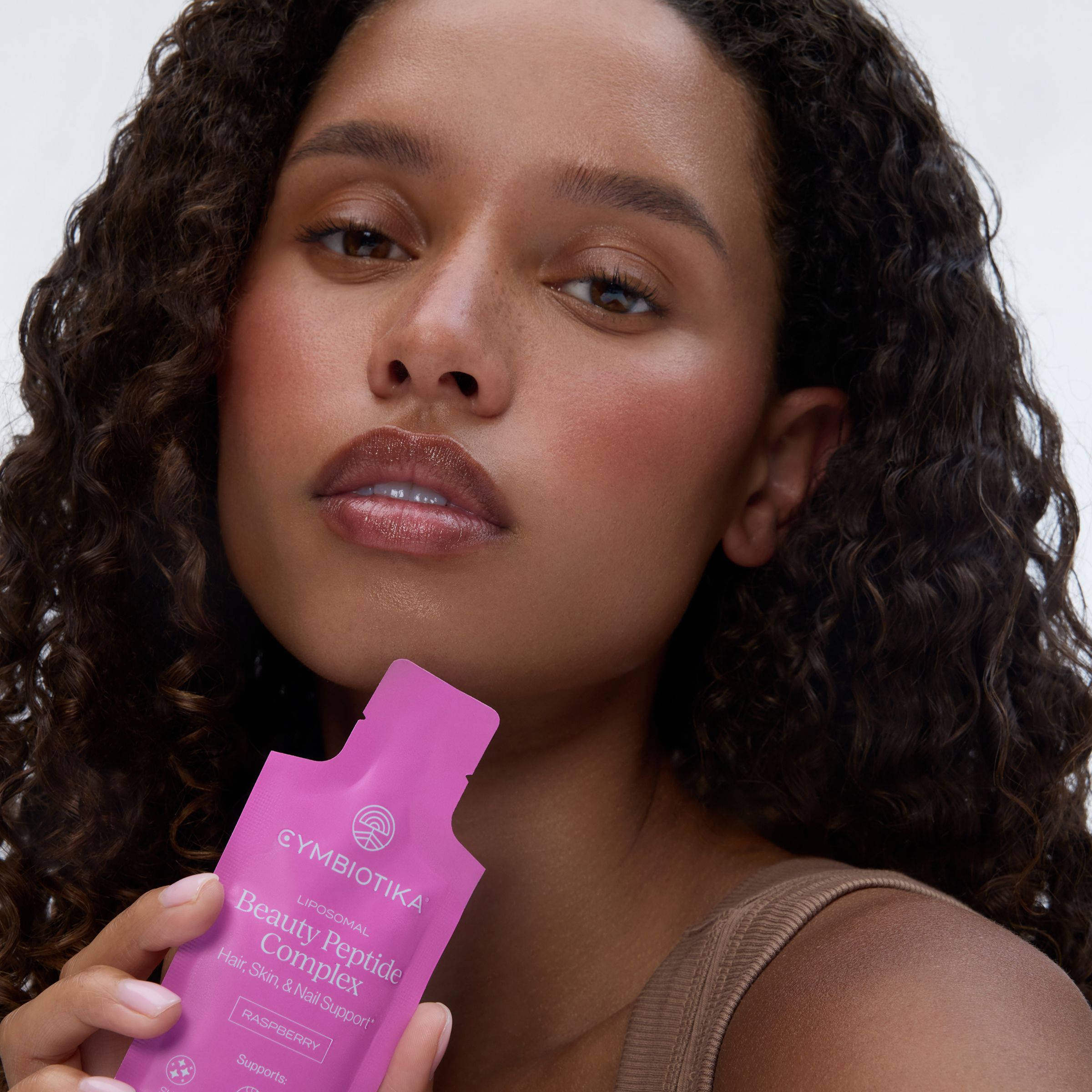 Woman holding a pink Cymbiotika Liposomal Beauty Peptide Complex sachet near her face.