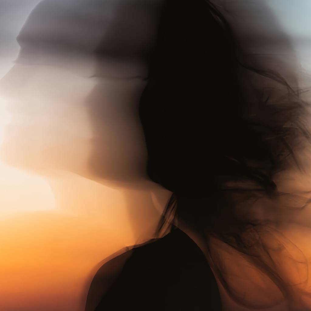 Blurred side profile of a woman with long dark hair against an orange sunset