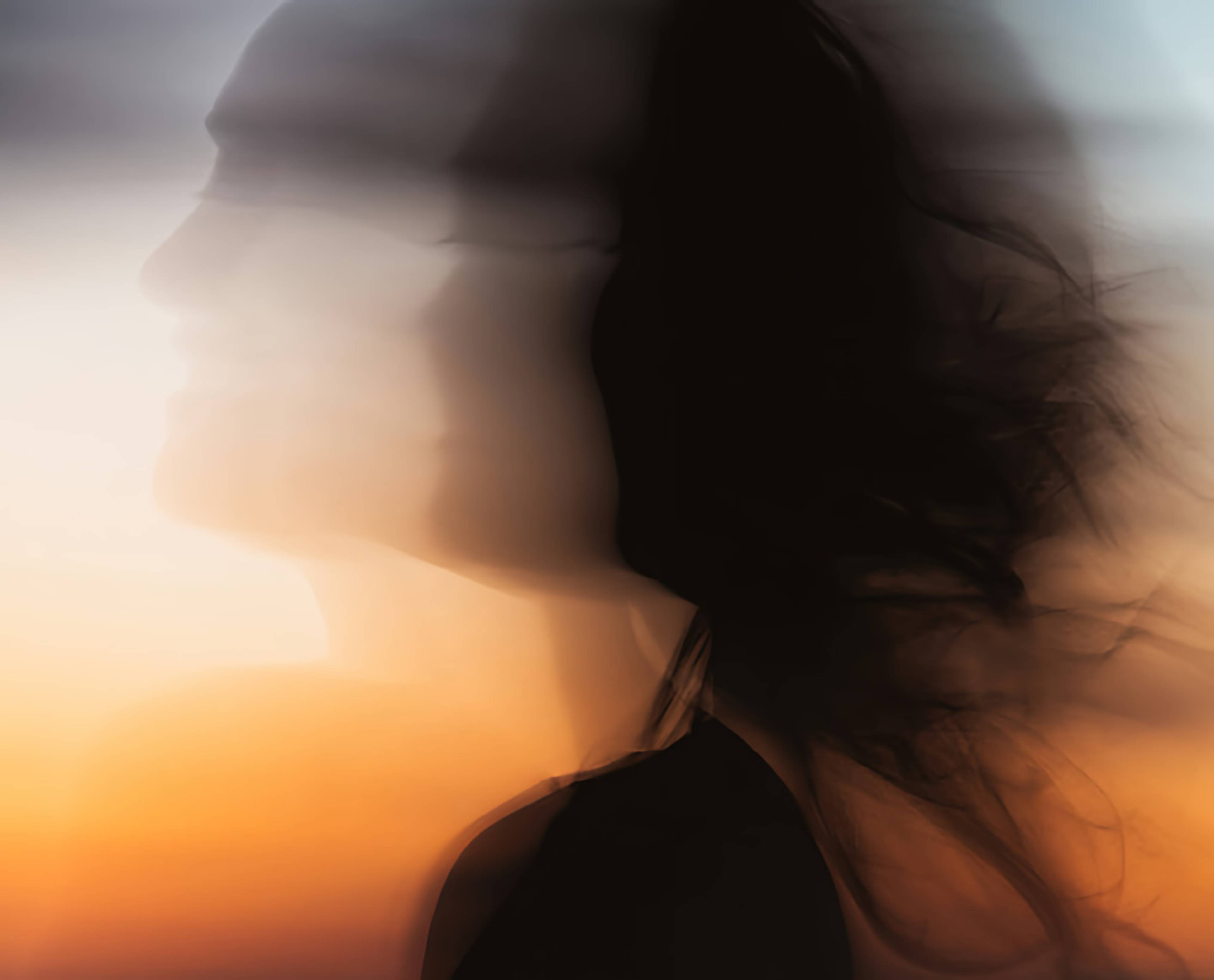 Blurred side profile of a woman with long dark hair against an orange sunset