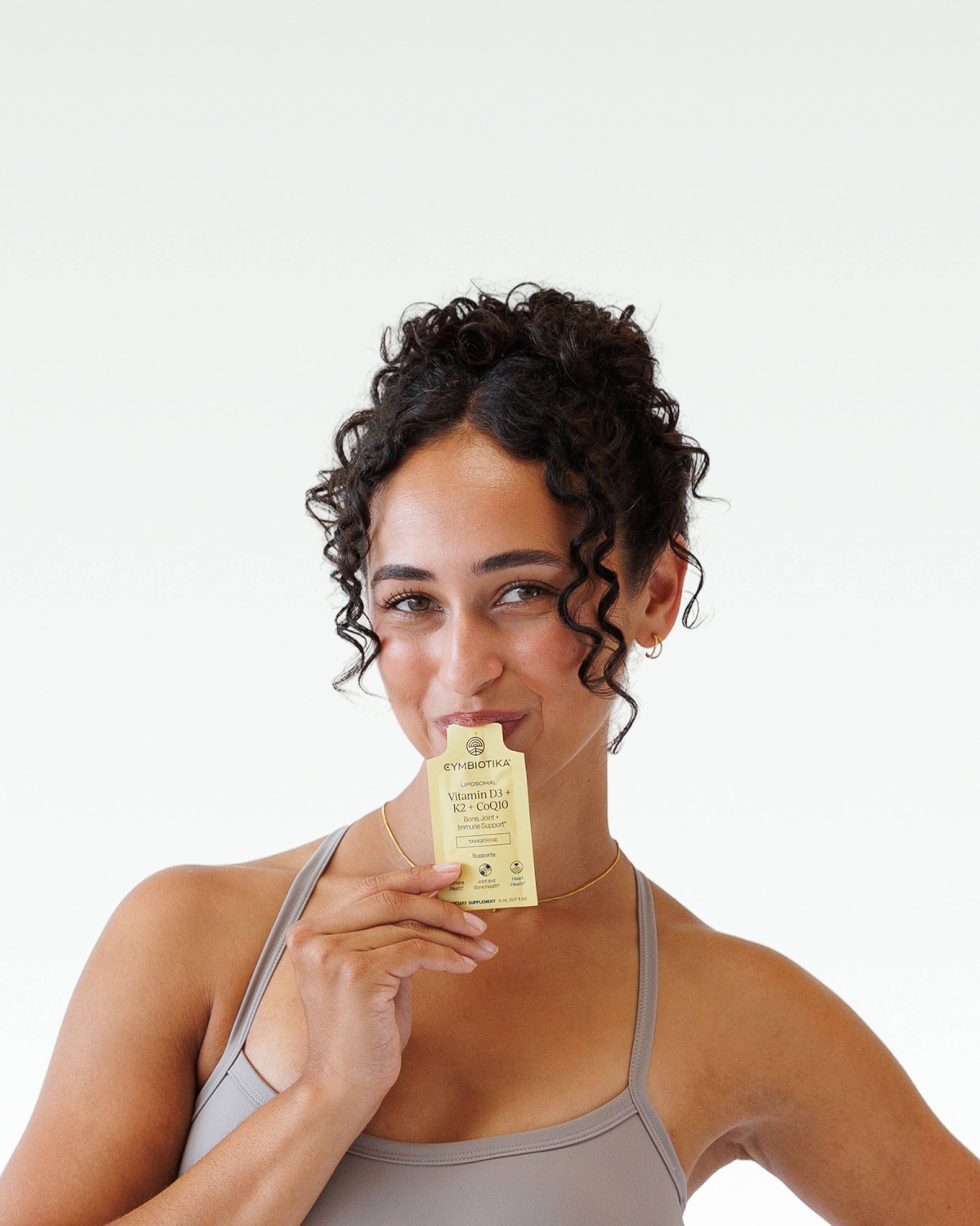 Woman holding a yellow Cymbiotika Vitamin D3 + K2 + CoQ10 sachet in front of her face.