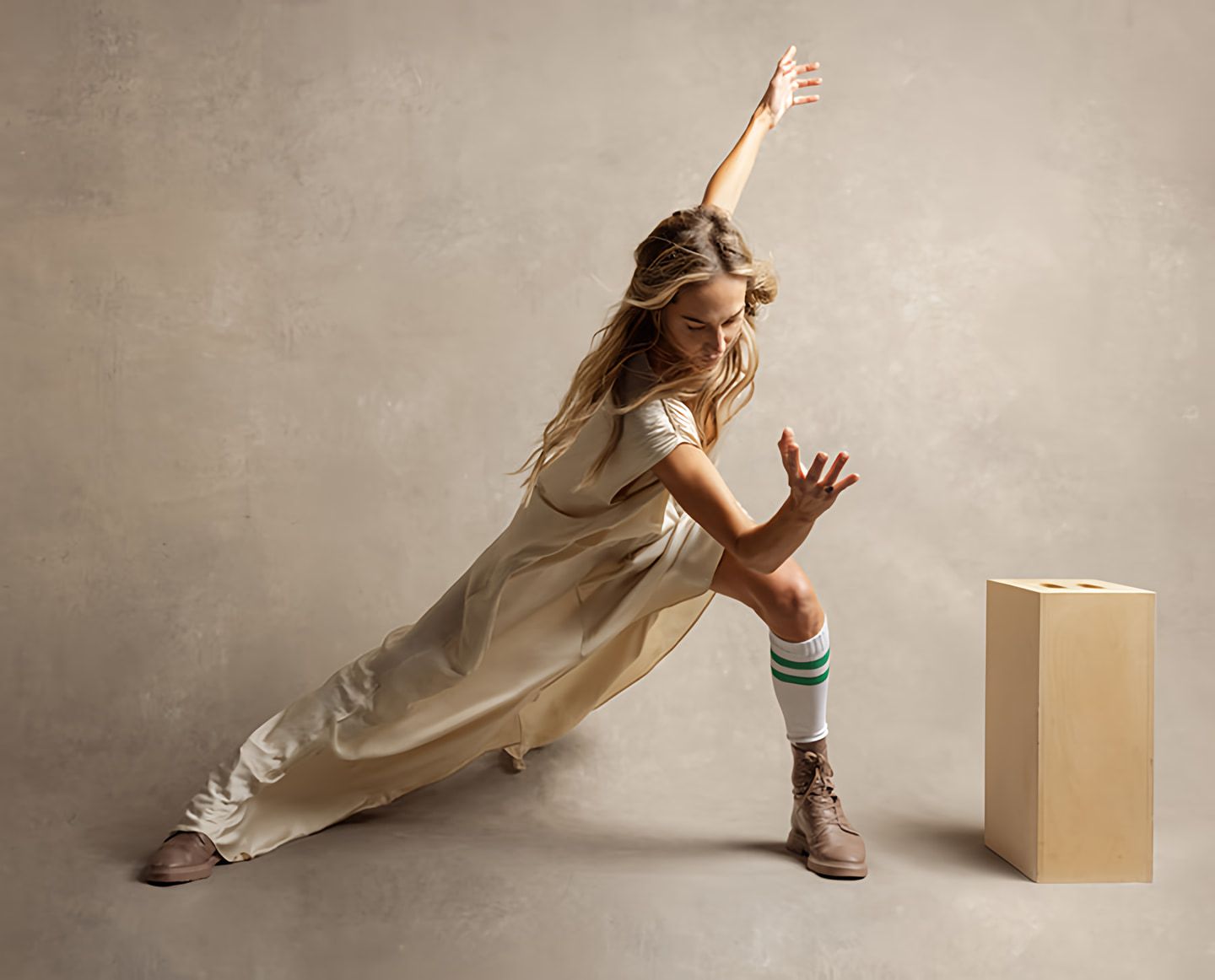 Woman in a cream dress holds a deep side lunge with one arm raised beside a wooden block.