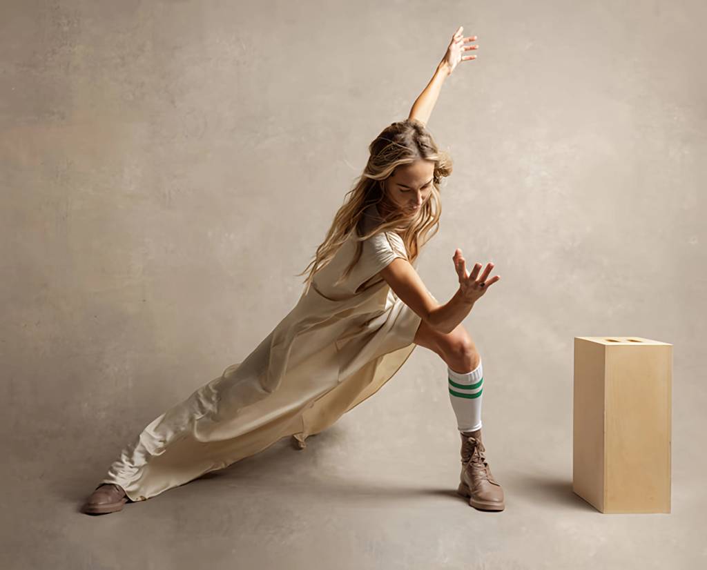 Woman in a cream dress holds a deep side lunge with one arm raised beside a wooden block.