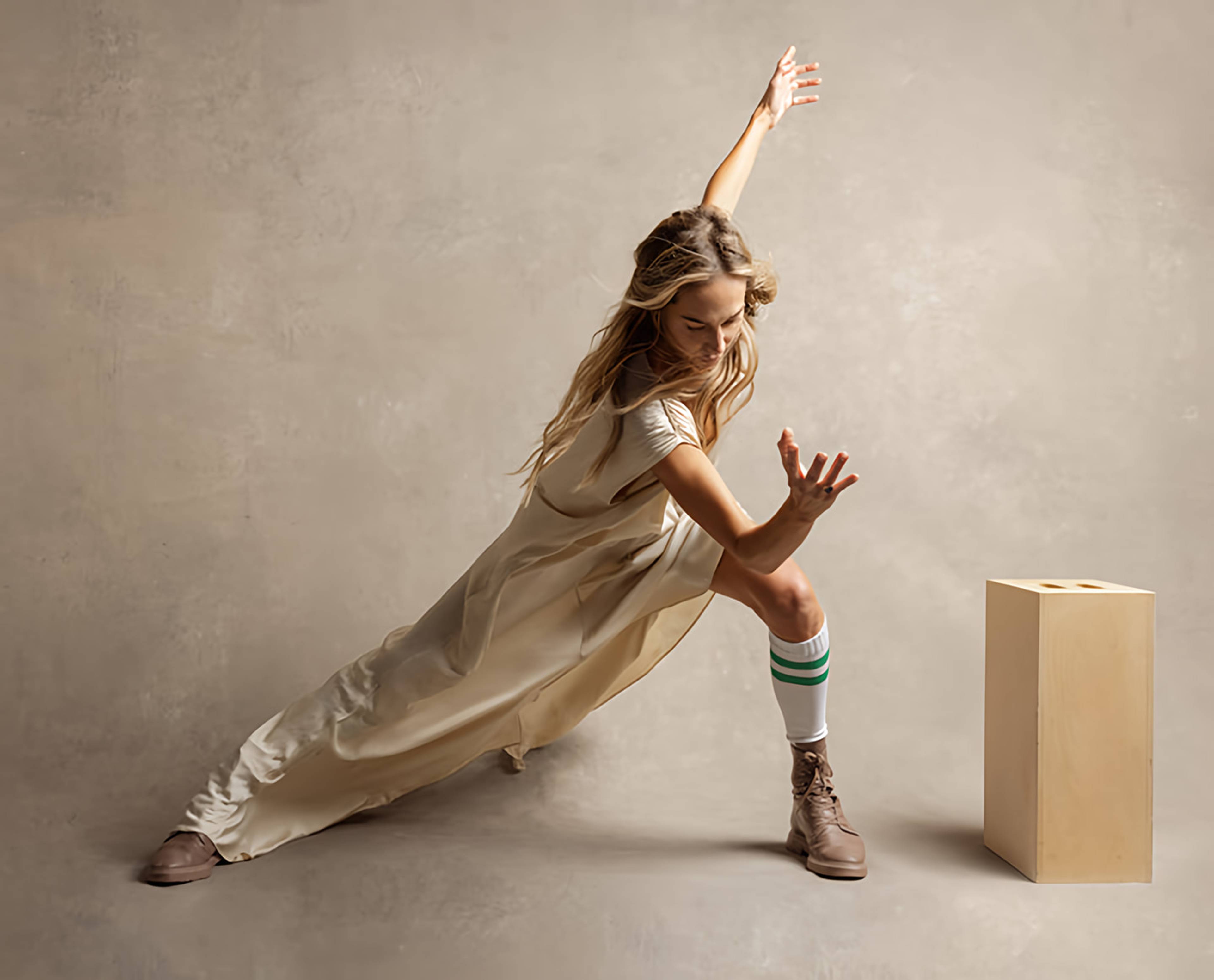 Woman in a cream dress holds a deep side lunge with one arm raised beside a wooden block.