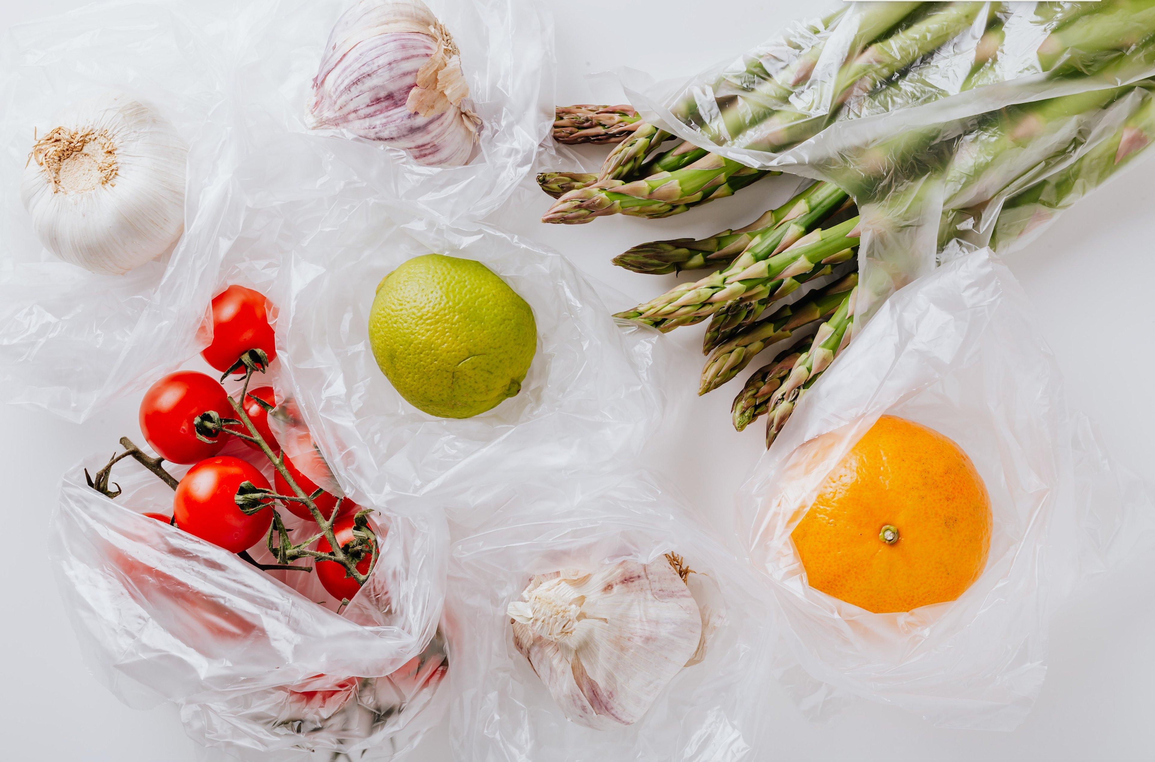 Garlic, tomatoes, a lime, an orange, and asparagus in clear plastic bags.