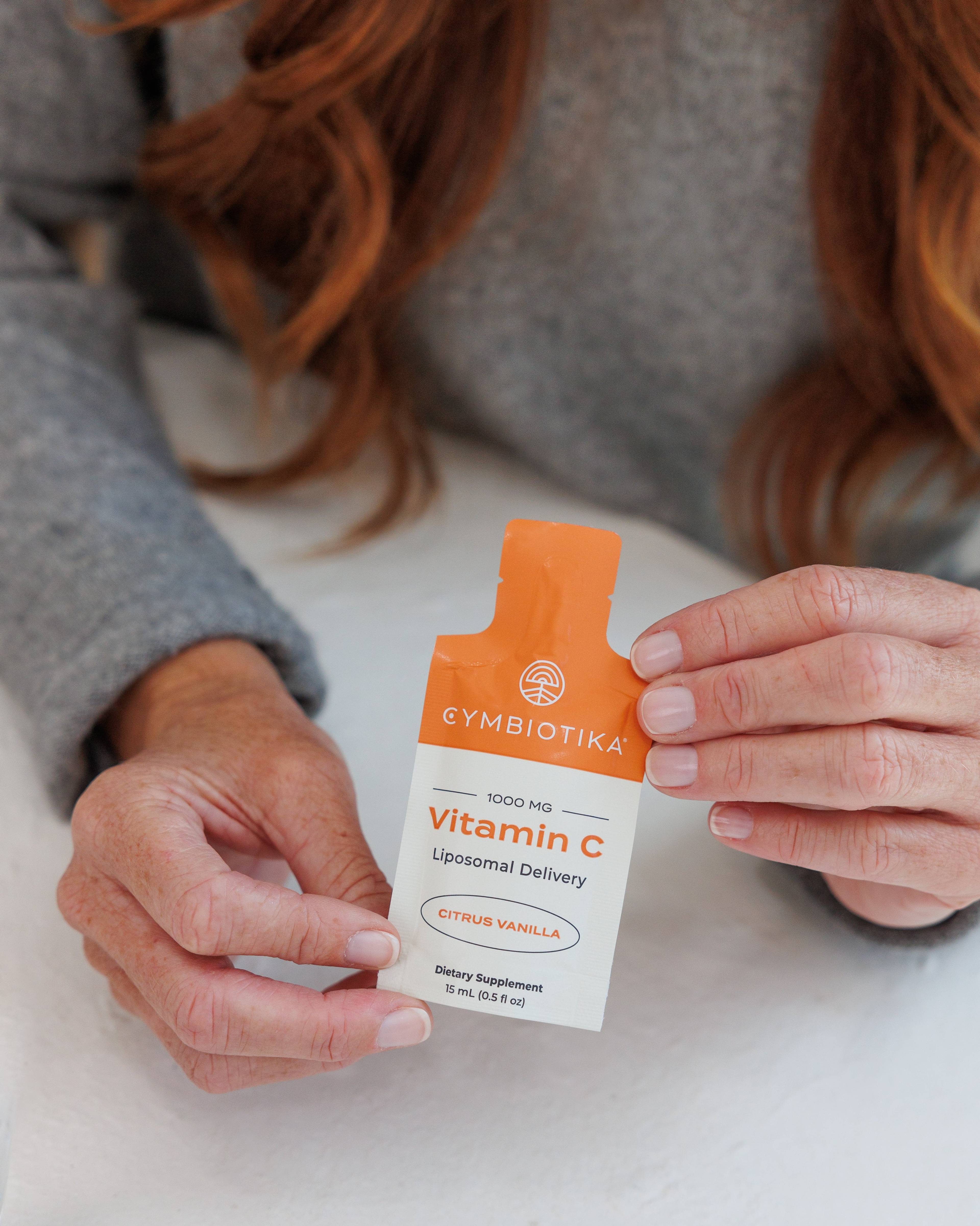 Person in a gray sweater holding a Cymbiotika Liposomal Vitamin C citrus vanilla packet.