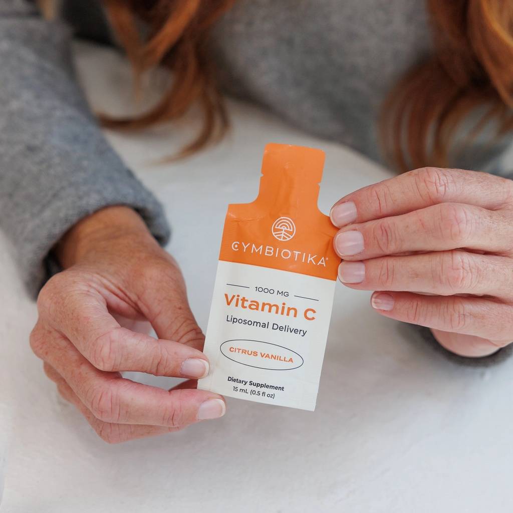 Person in a gray sweater holding a Cymbiotika Liposomal Vitamin C citrus vanilla packet.