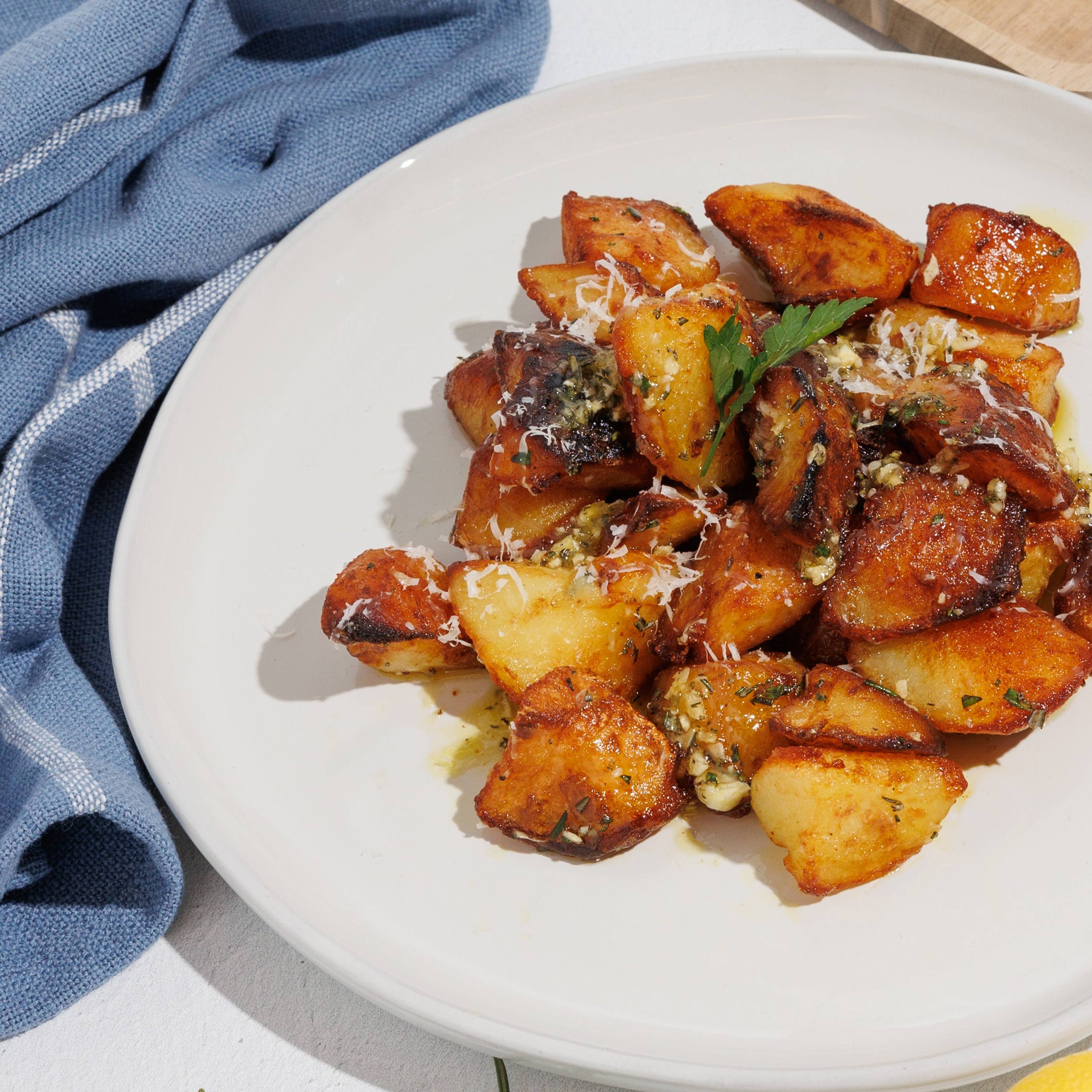 Plate of crispy herb-roasted potato bites with grated cheese, rosemary, lemon, and a wedge of cheese nearby.
