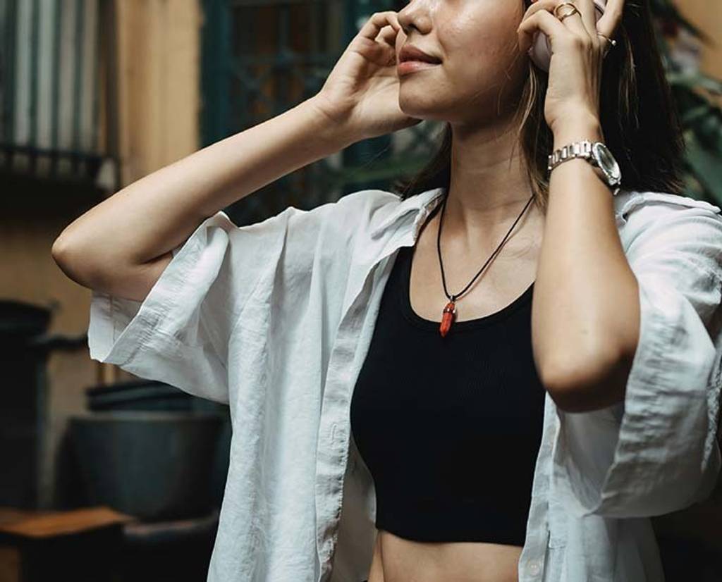Woman in a white shirt adjusts her hair indoors.