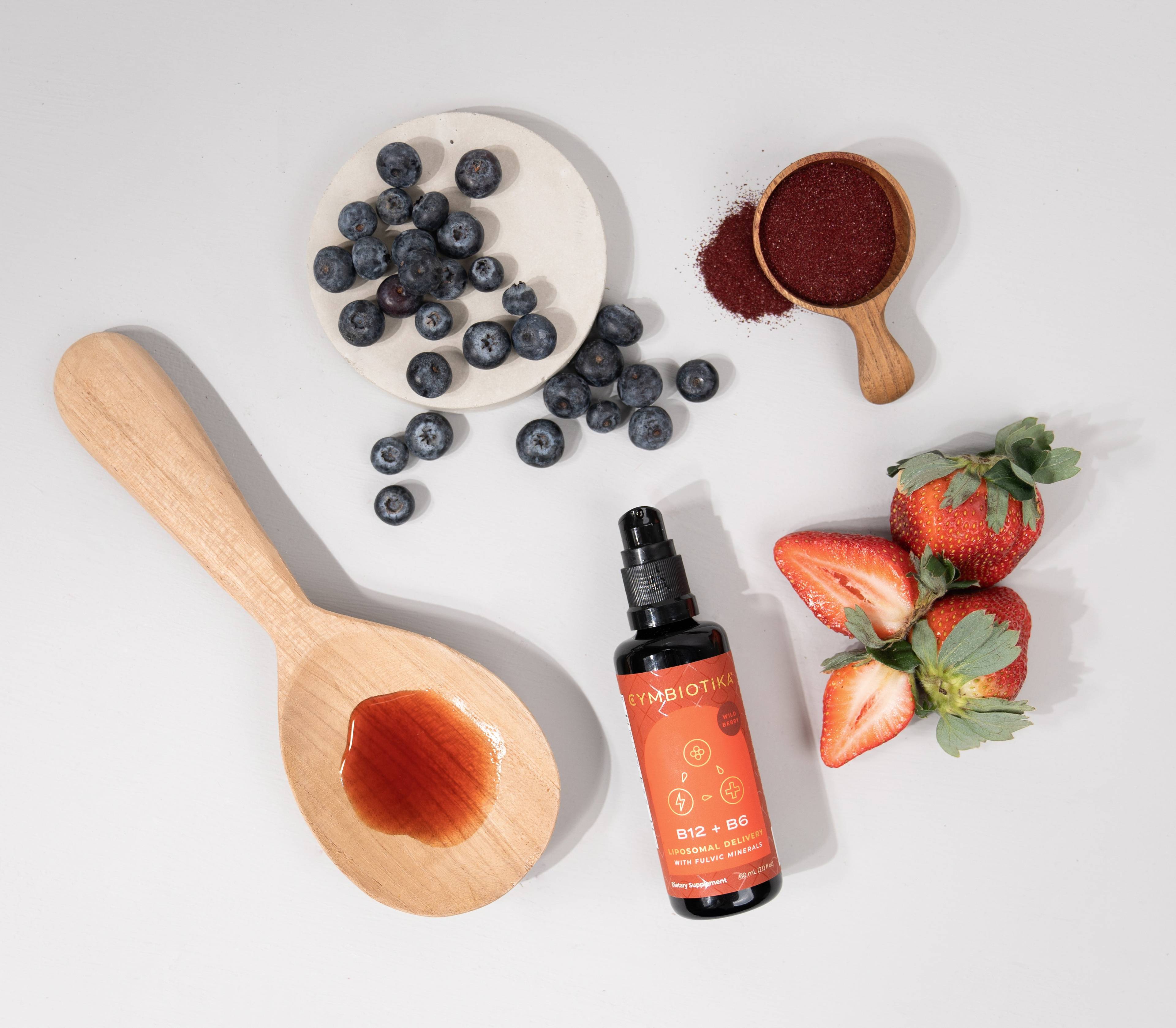 Cymbiotika B12 + B6 bottle with strawberries, blueberries, red powder, and two wooden spoons.