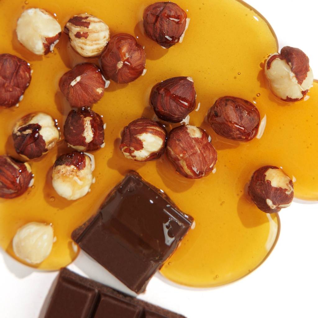 Hazelnuts and dark chocolate pieces in a pool of glossy amber liquid.