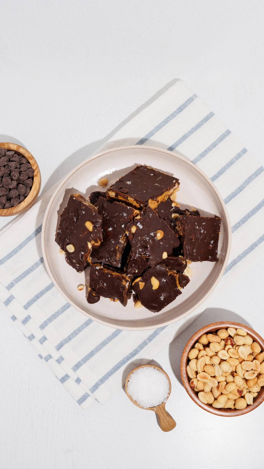 Plate of chocolate-coated peanut bars with bowls of chocolate chips, peanuts, and salt.