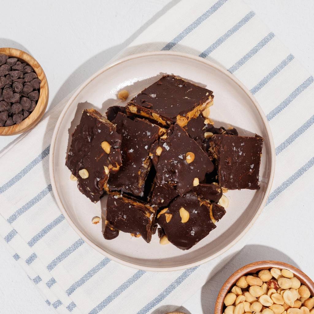 Plate of chocolate-coated peanut bars with bowls of chocolate chips, peanuts, and salt.