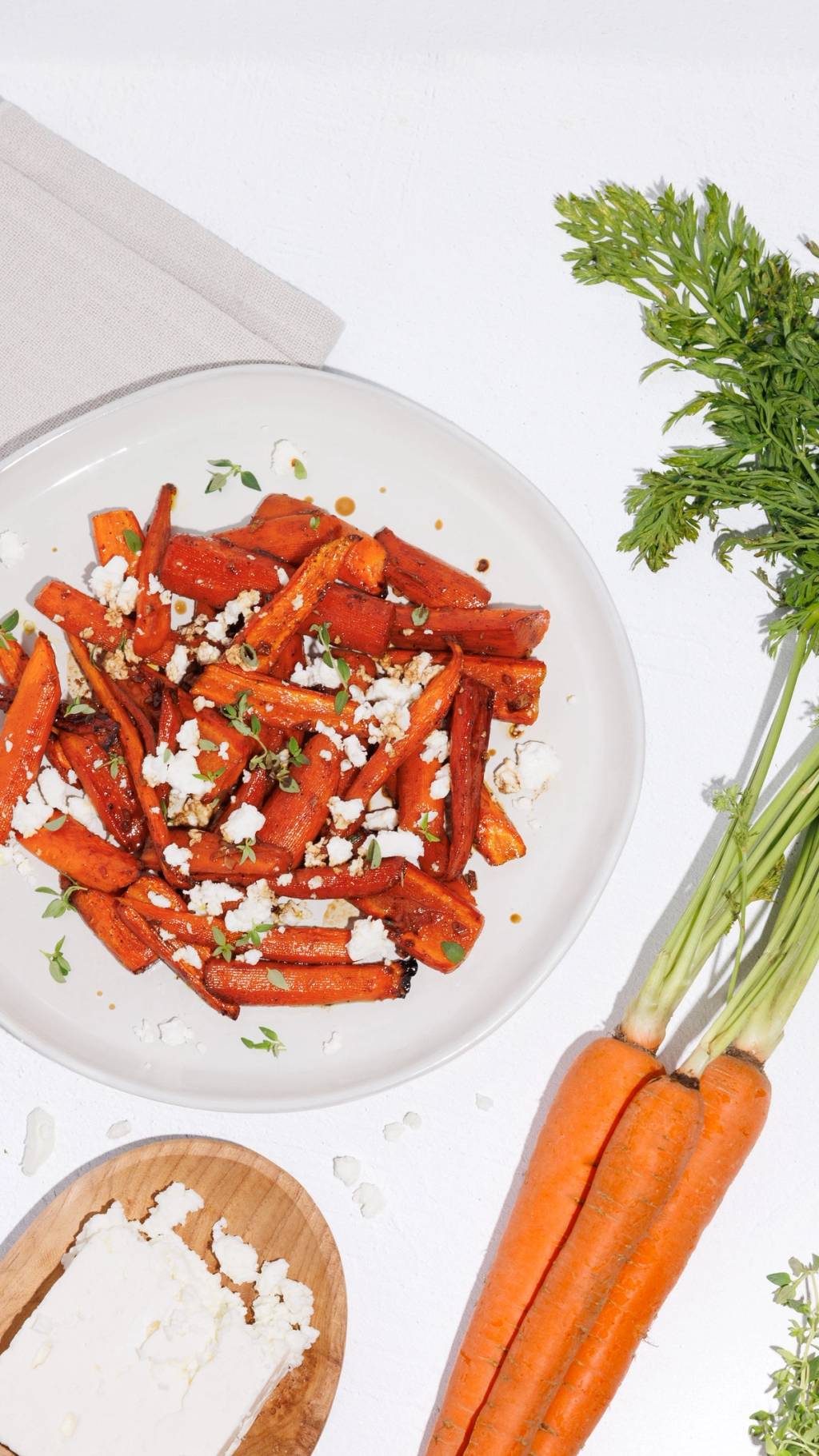 Roasted carrots with crumbled cheese and herbs on a white plate beside fresh carrots.