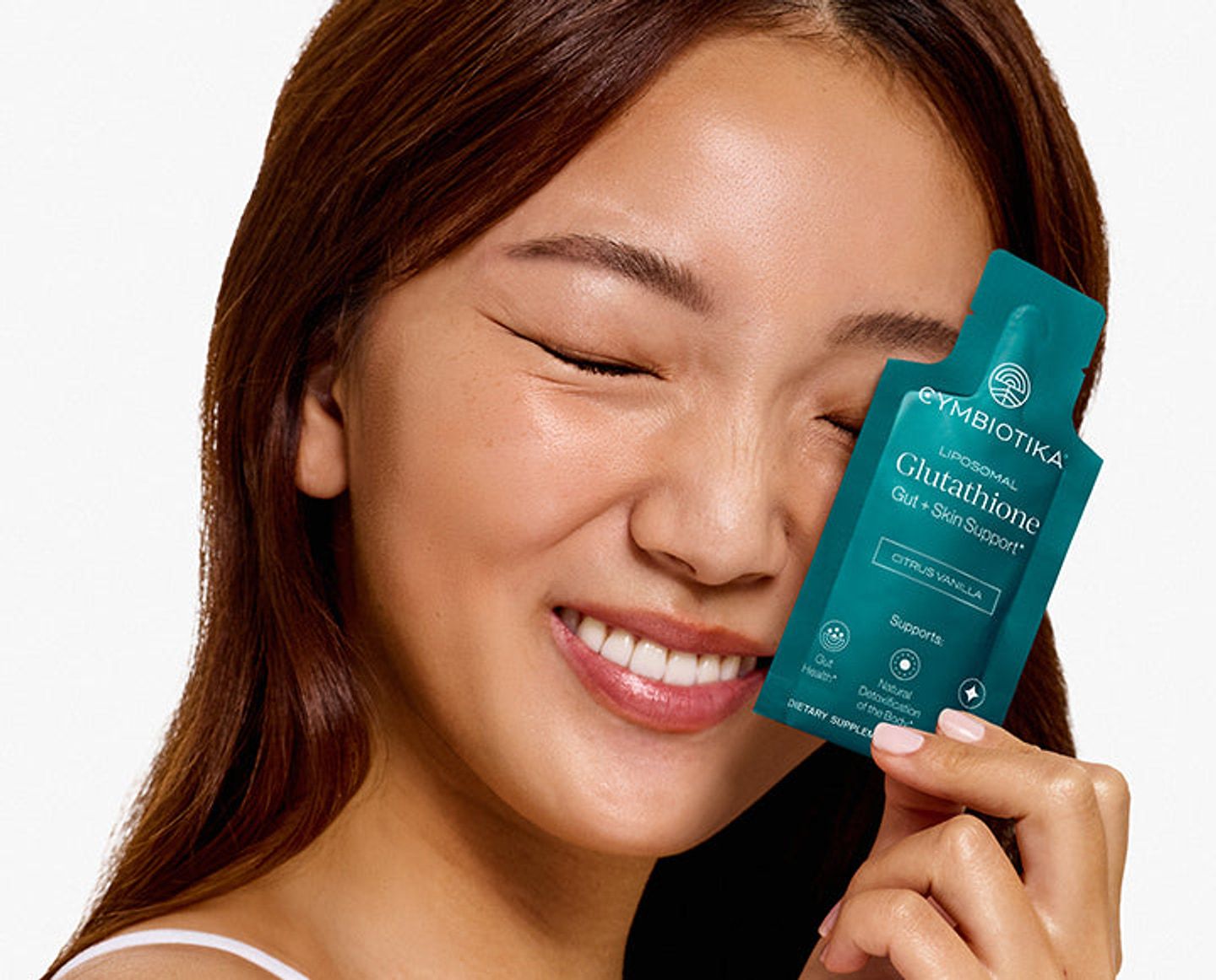 Smiling woman holding a Cymbiotika Liposomal Glutathione packet beside her face.