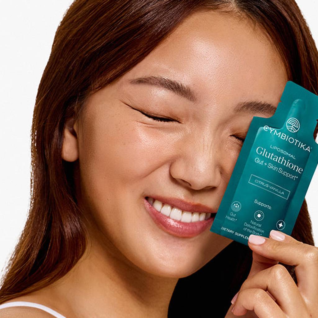 Smiling woman holding a Cymbiotika Liposomal Glutathione packet beside her face.
