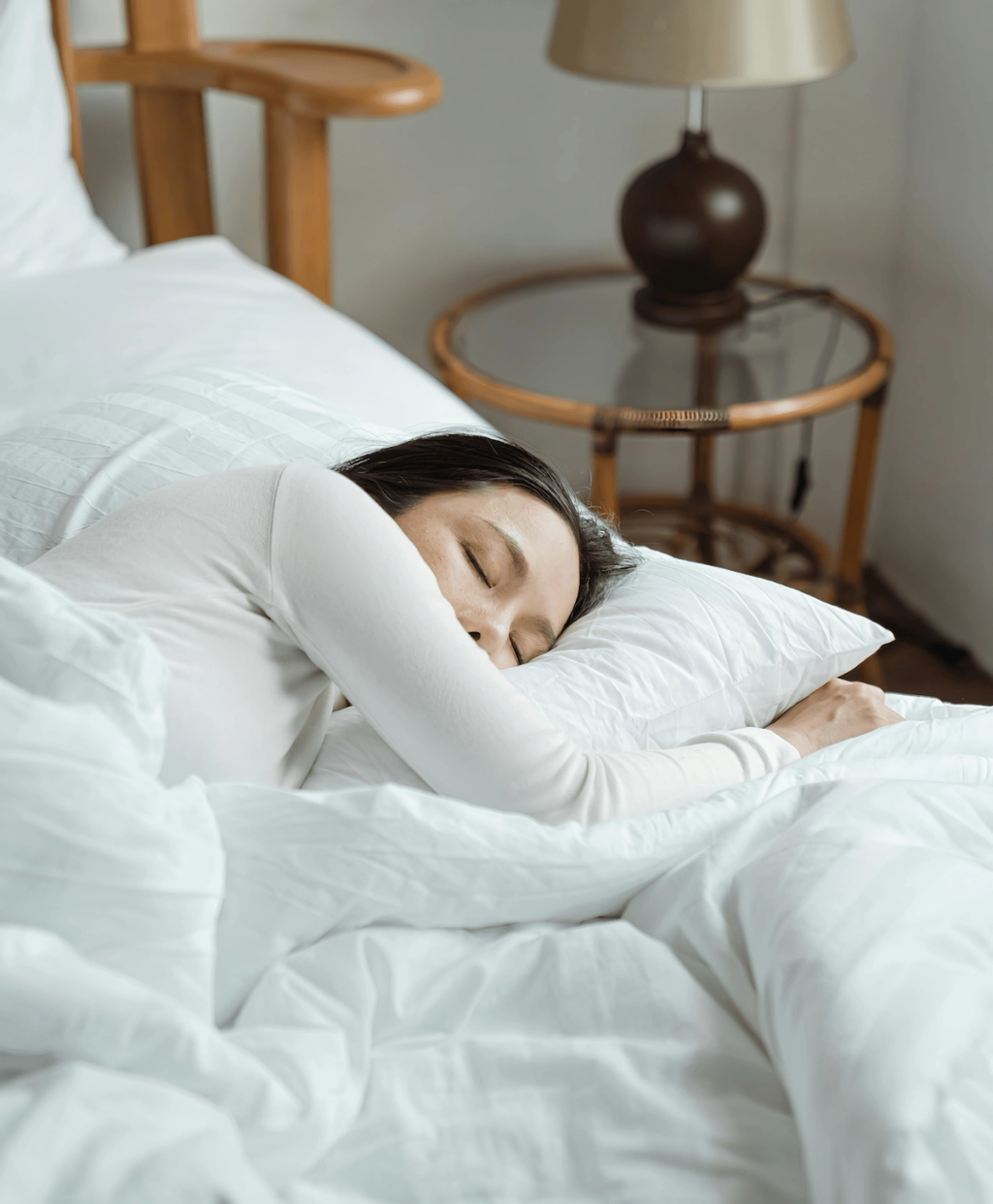Woman sleeping on her side in a white bed beside a bedside lamp.