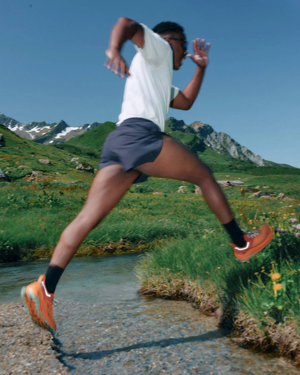 Runner leaps across a shallow stream in a mountain meadow.