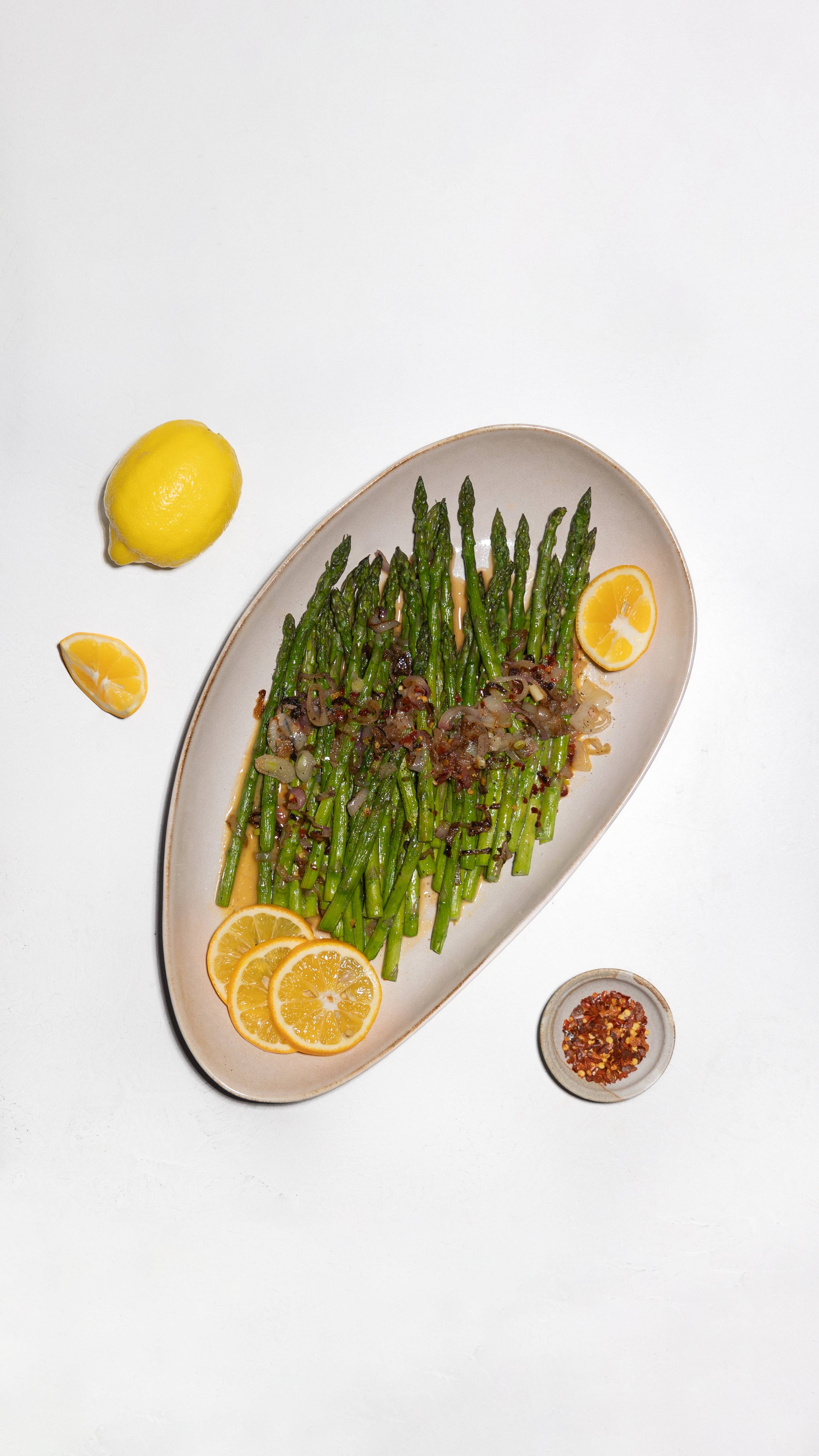 Asparagus topped with browned pieces and lemon slices on an oval plate.