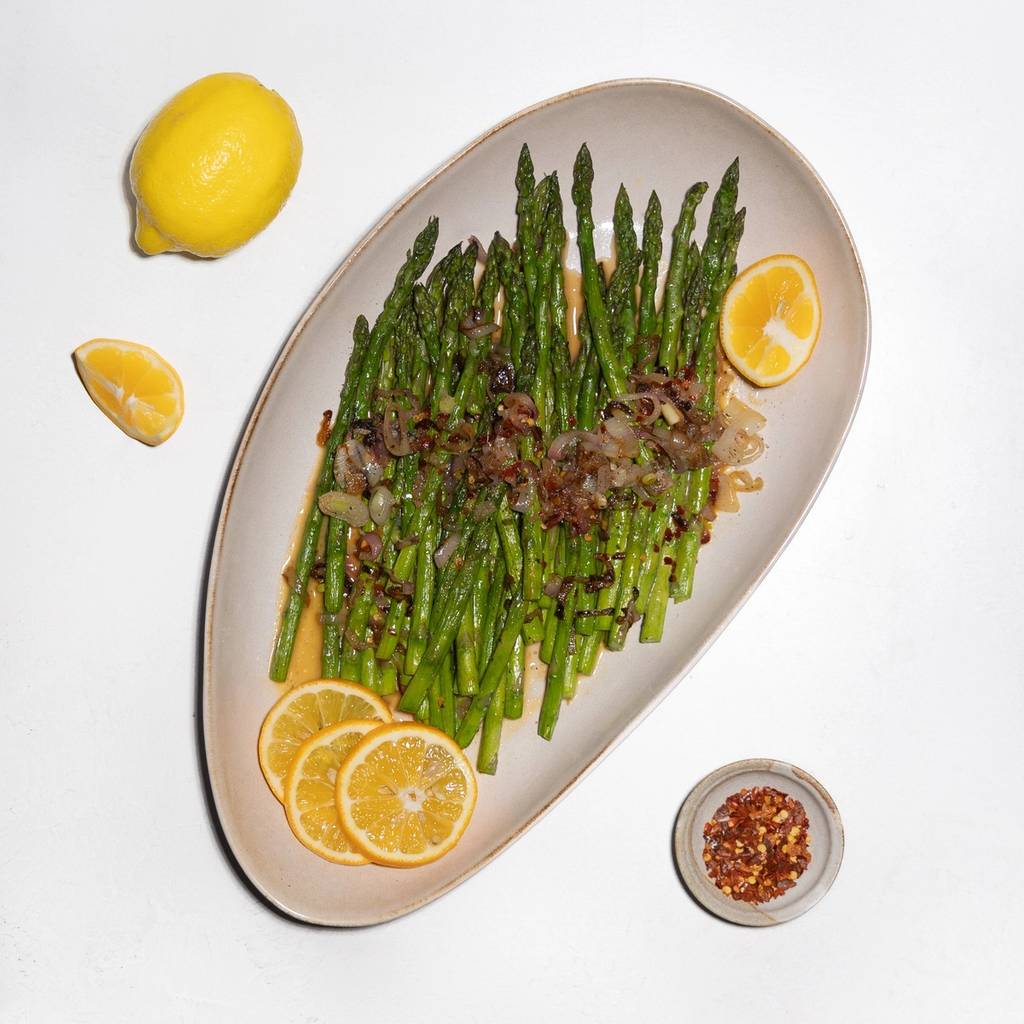 Asparagus topped with browned pieces and lemon slices on an oval plate.
