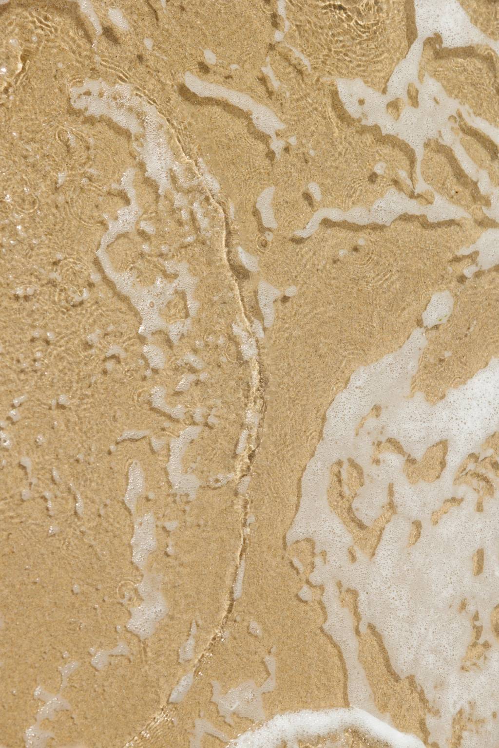 Close-up of a tan, textured surface streaked with white foam and moisture.