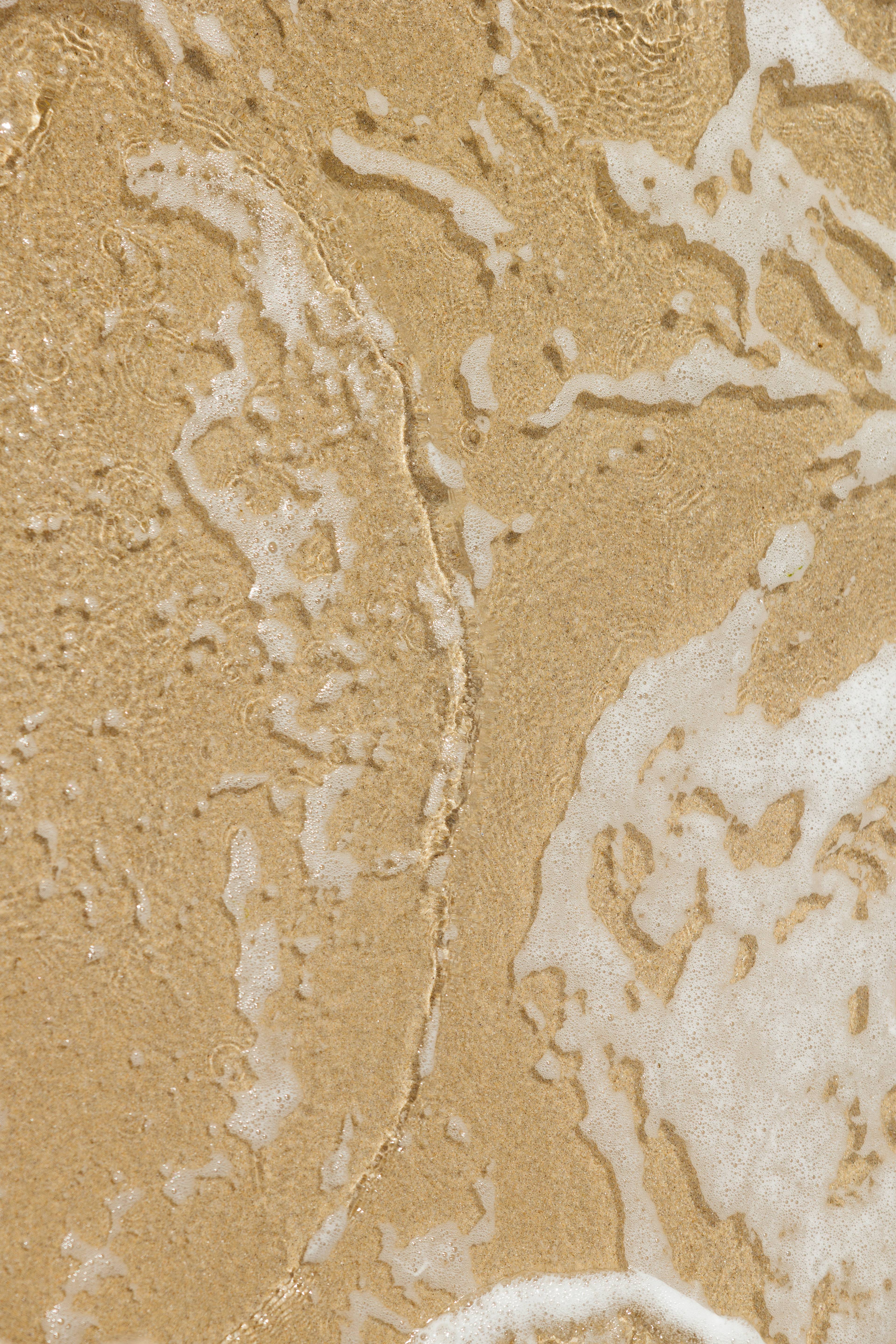 Close-up of a tan, textured surface streaked with white foam and moisture.