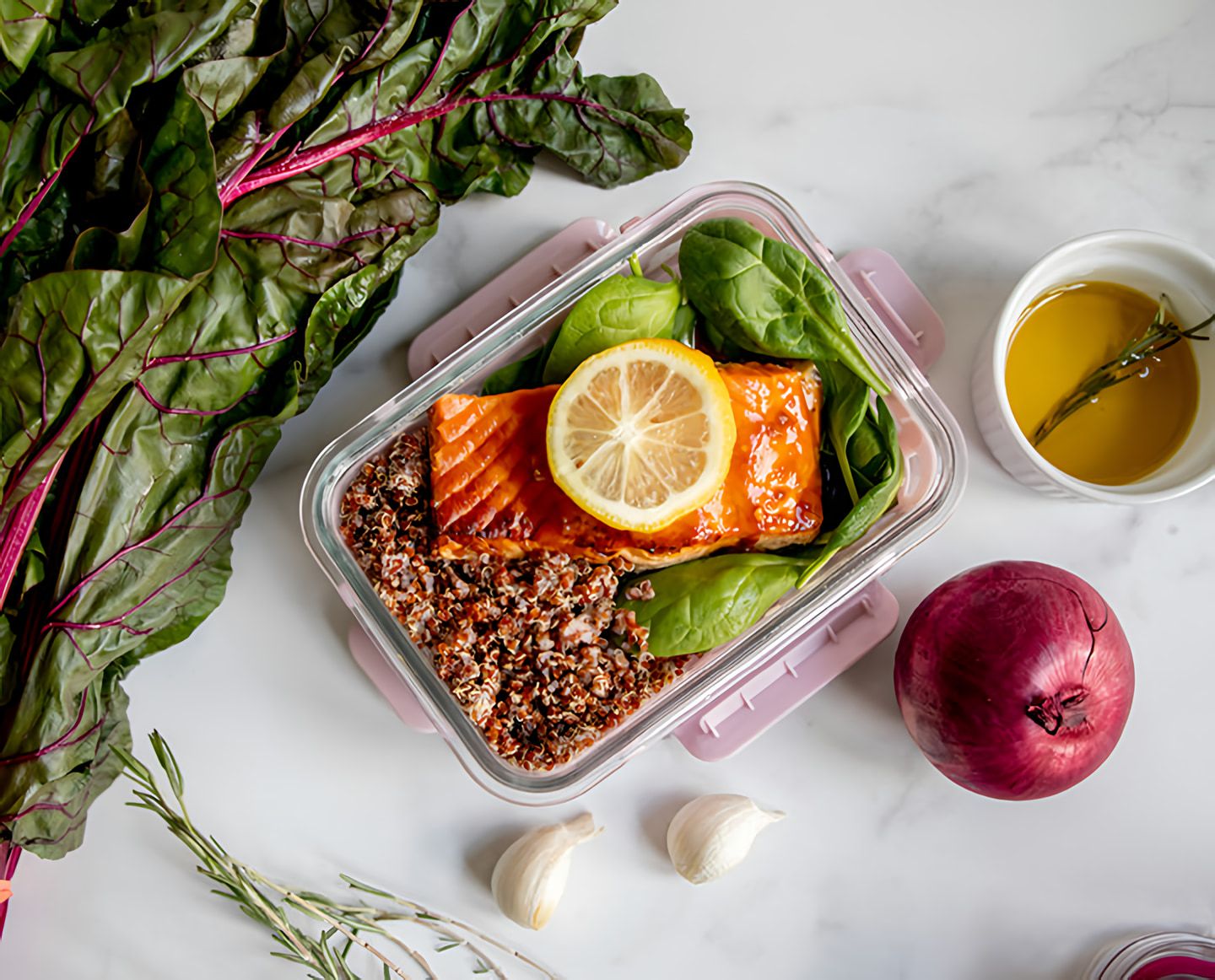 Salmon with lemon, quinoa, spinach, leafy greens, garlic, and red onion, with a bowl of oil beside it.