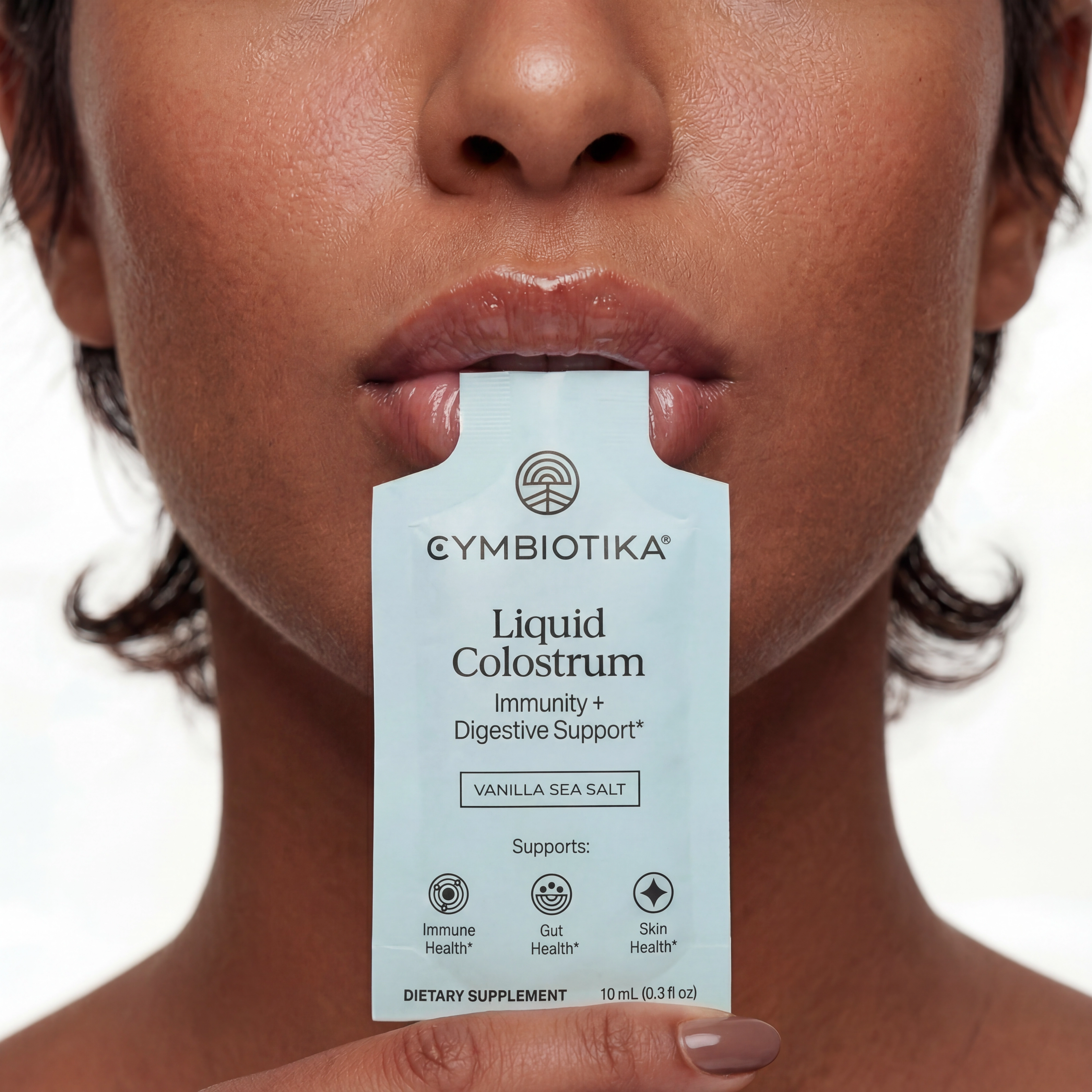 A person holds a Liquid Colostrum sachet to their lips, demonstrating how to take the product directly from the packet.