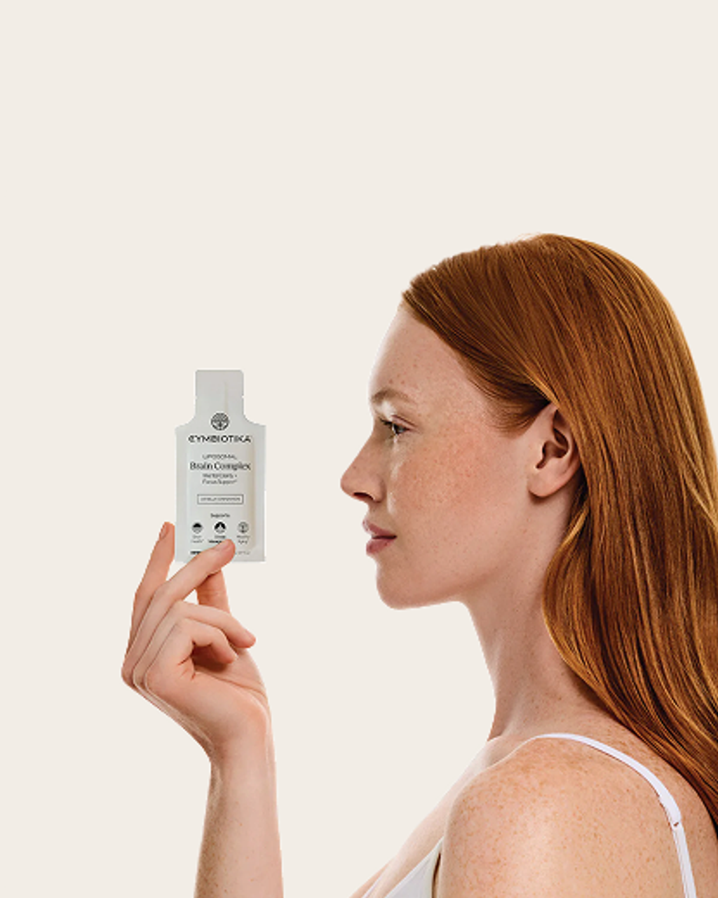 Woman holding a small white Brain Complex supplement package beside her face.