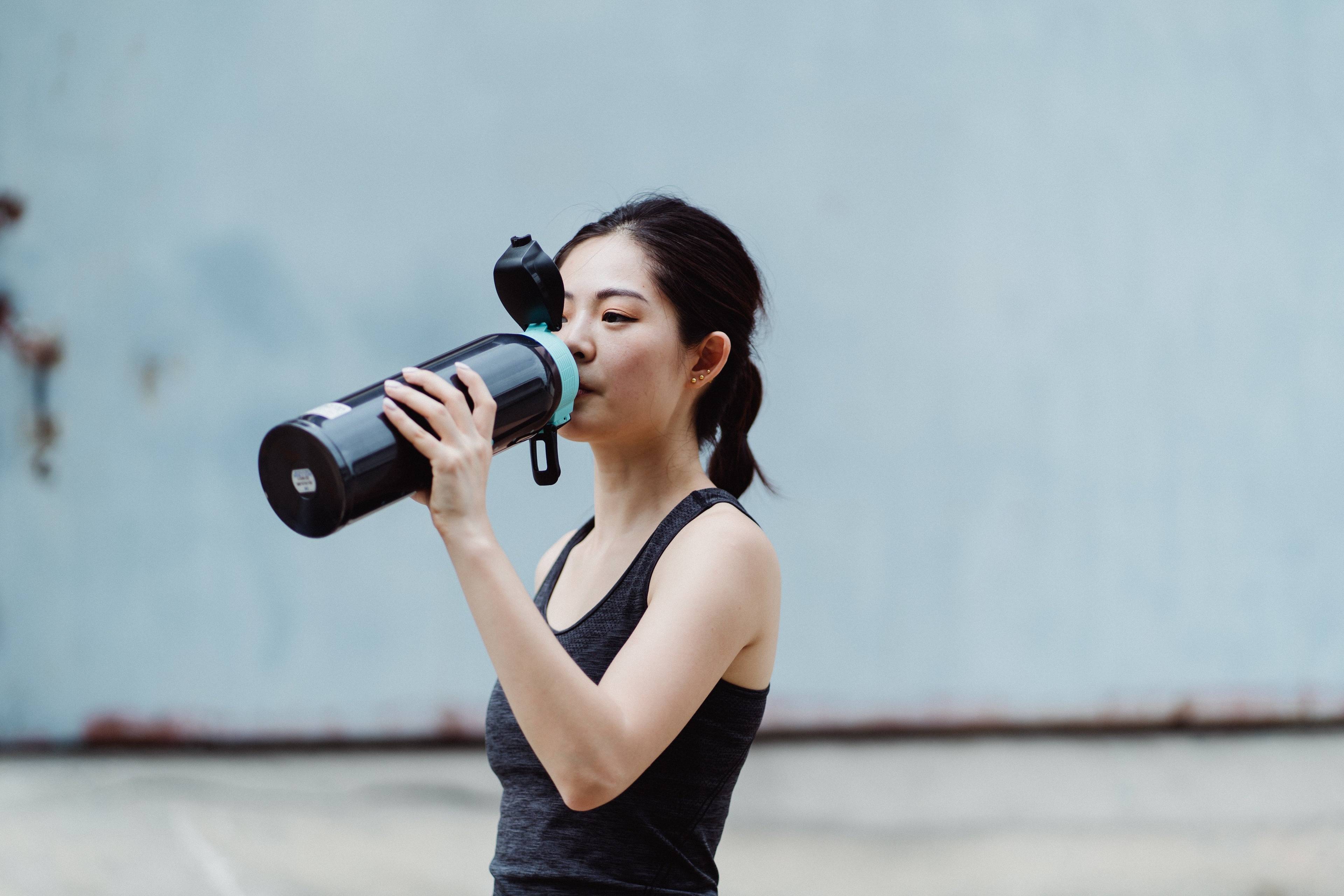 Woman in athletic wear drinking from a black reusable water bottle outdoors.