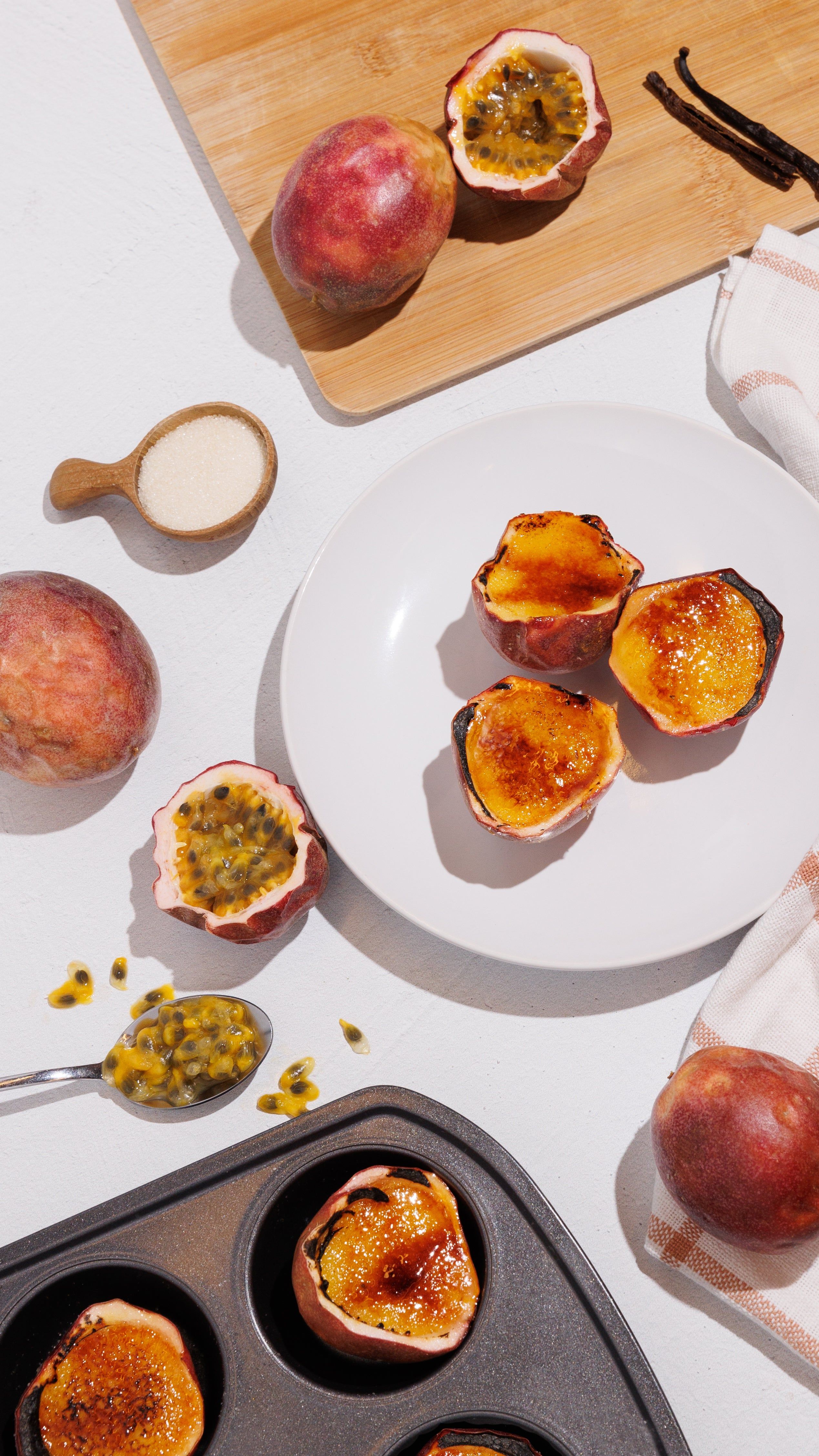 Overhead view of caramelized passion fruit desserts in fruit shells with fresh passion fruit, sugar, and vanilla beans.