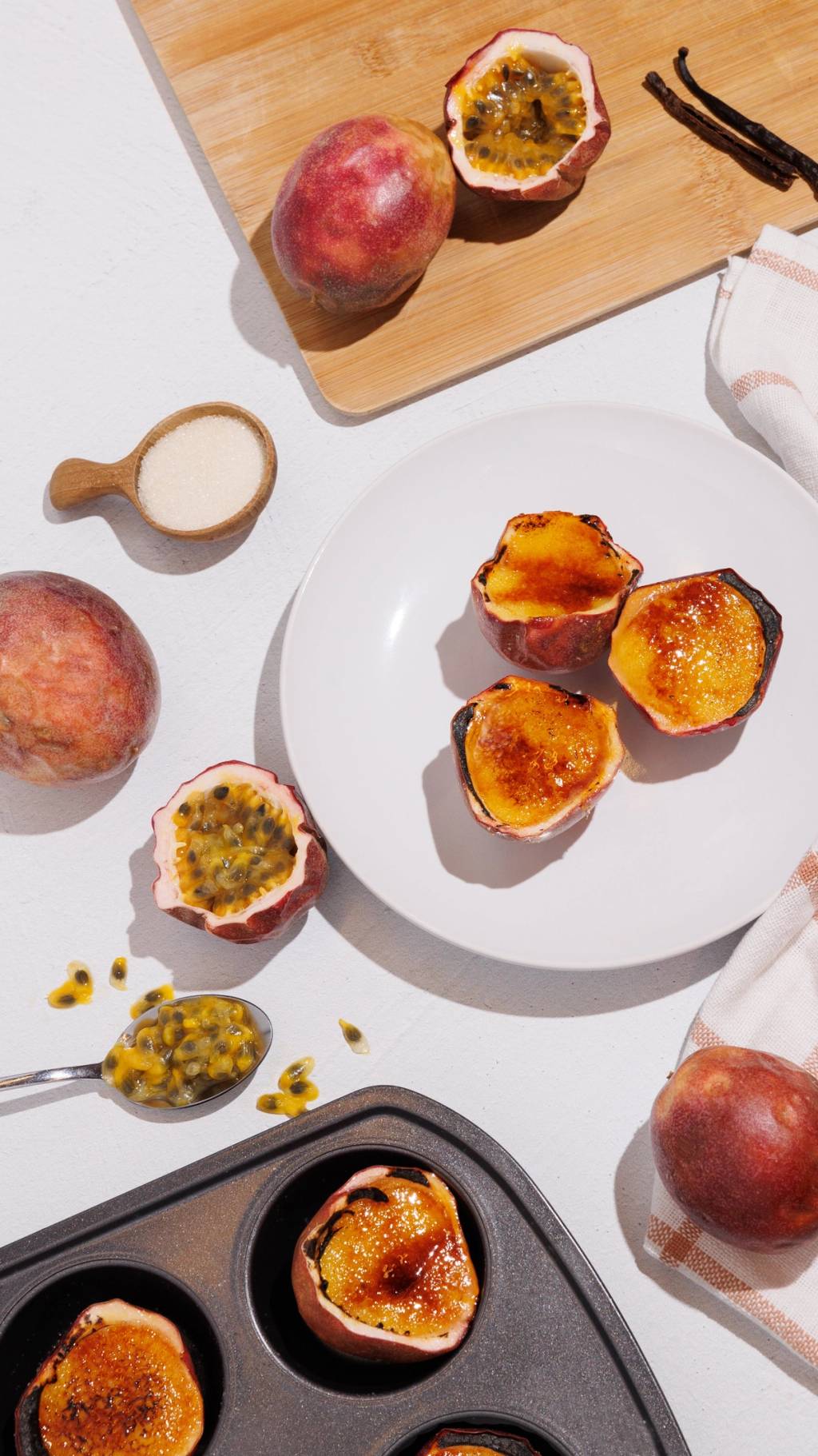 Overhead view of caramelized passion fruit desserts in fruit shells with fresh passion fruit, sugar, and vanilla beans.