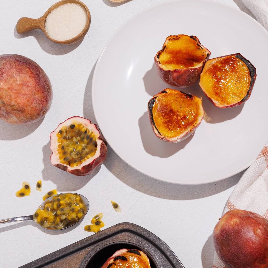 Overhead view of caramelized passion fruit desserts in fruit shells with fresh passion fruit, sugar, and vanilla beans.