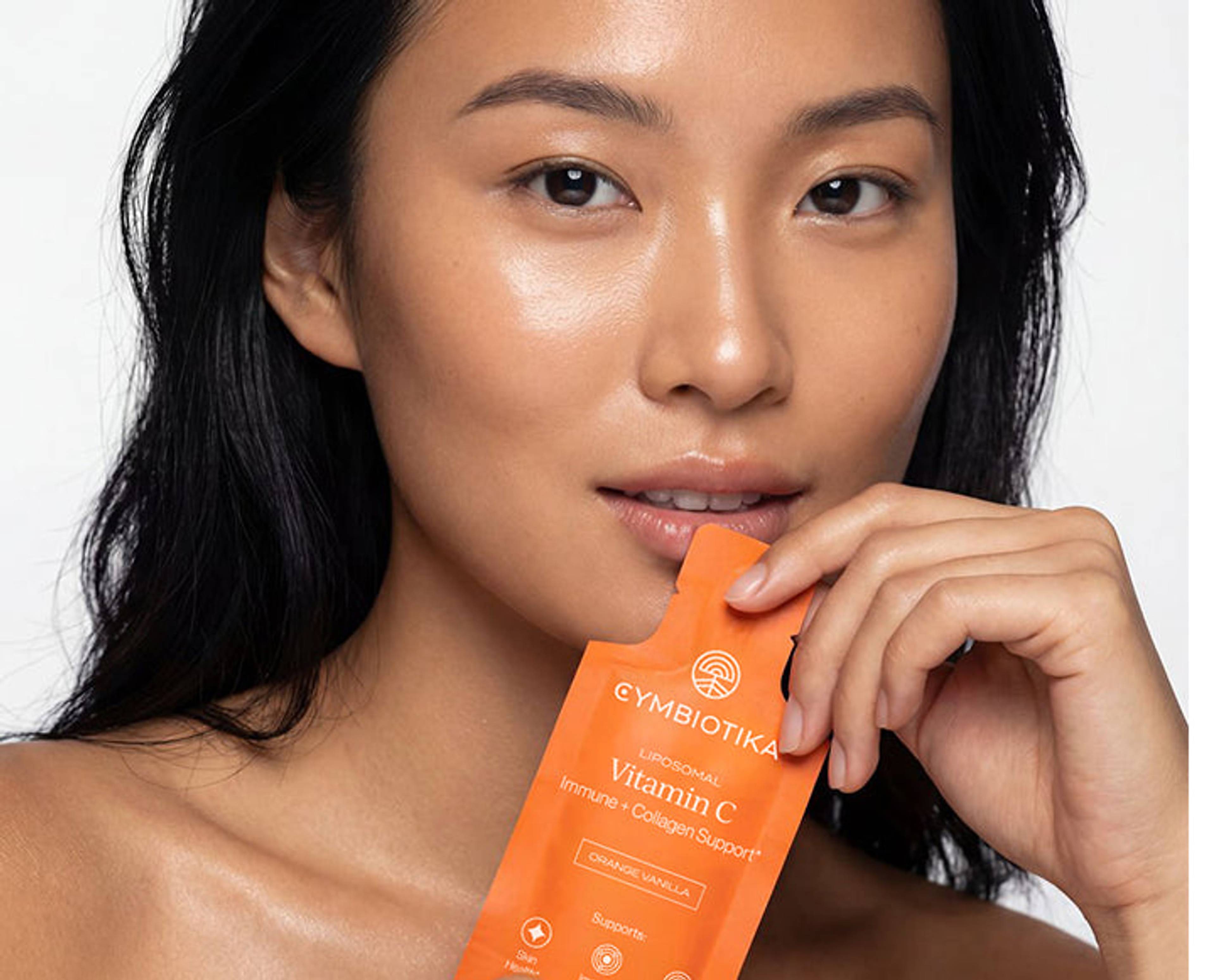 Woman holding a Cymbiotika Liposomal Vitamin C packet near her mouth.