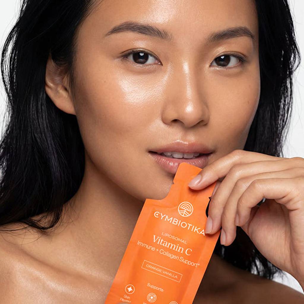 Woman holding a Cymbiotika Liposomal Vitamin C packet near her mouth.