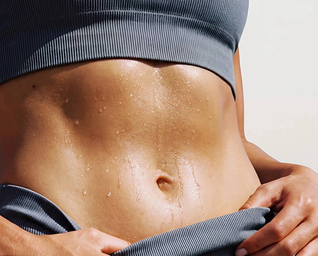 Close-up of a person's sweaty abdomen in gray ribbed workout clothing.