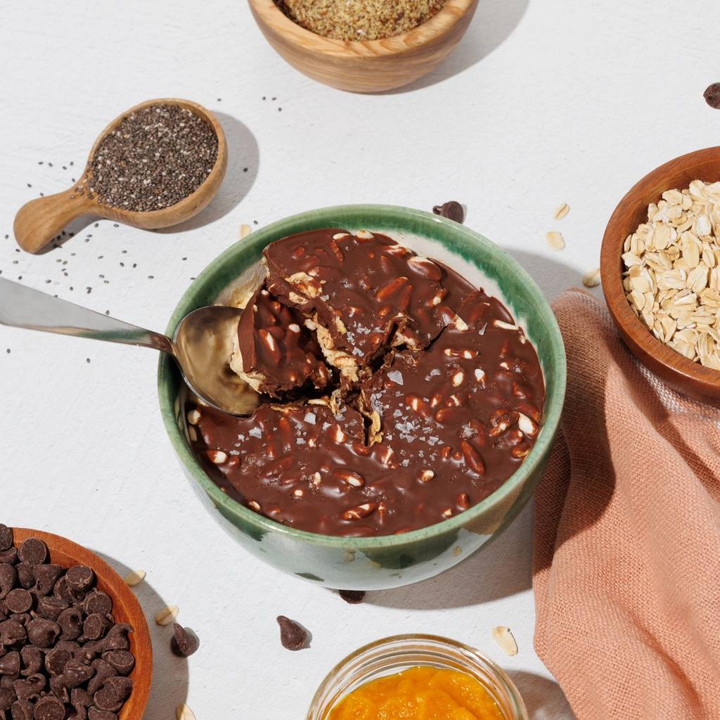 Bowl of chocolate overnight oats with a spoon, surrounded by pumpkin puree, chia seeds, rolled oats, and chocolate chips.