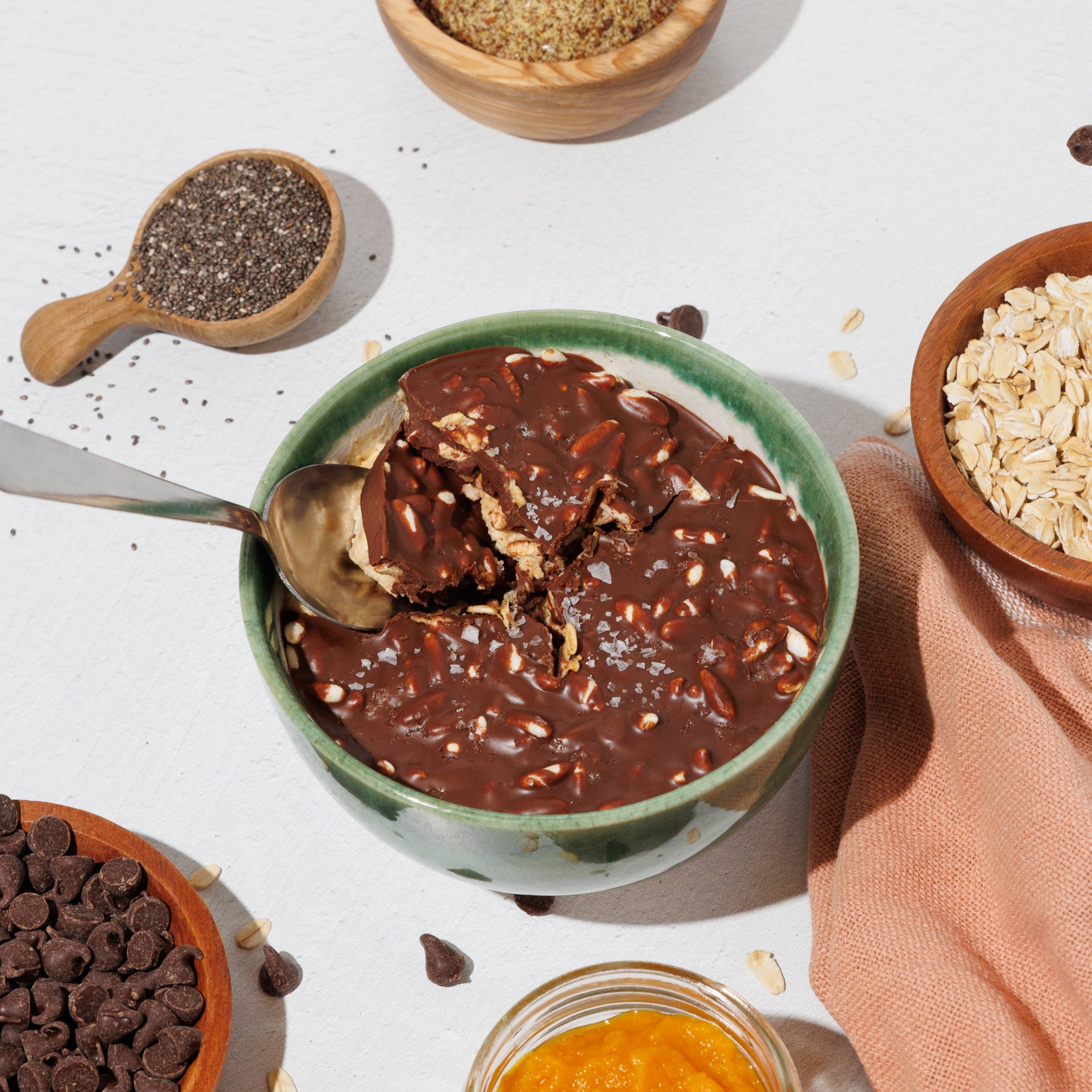 Bowl of chocolate overnight oats with a spoon, surrounded by pumpkin puree, chia seeds, rolled oats, and chocolate chips.