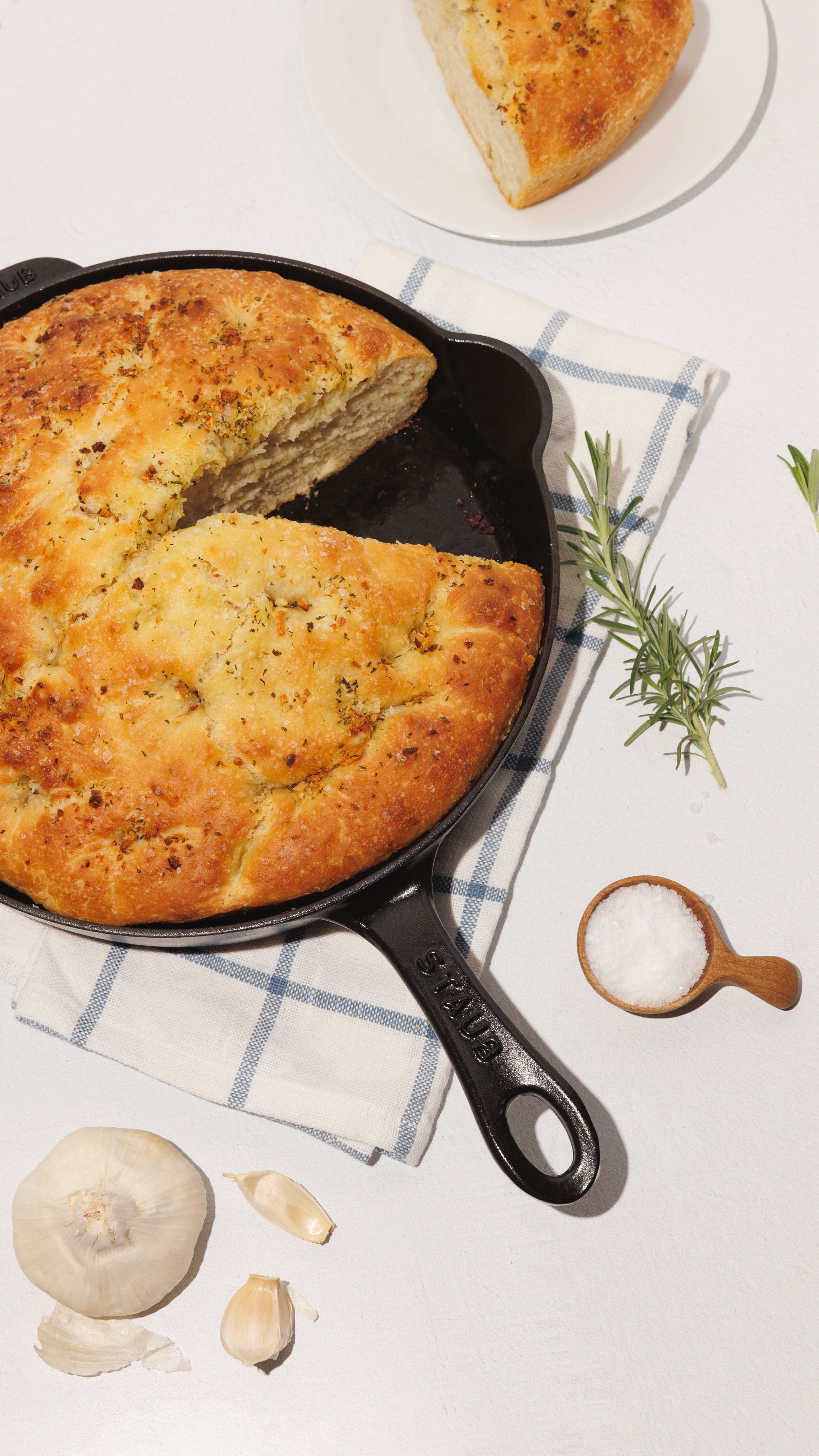 Rosemary focaccia in a cast-iron skillet with garlic, salt, and fresh rosemary.