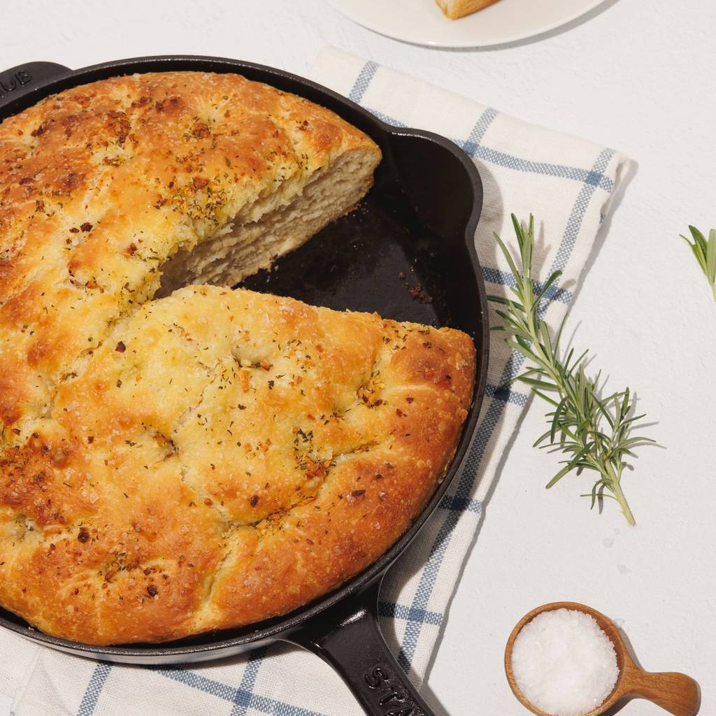 Rosemary focaccia in a cast-iron skillet with garlic, salt, and fresh rosemary.
