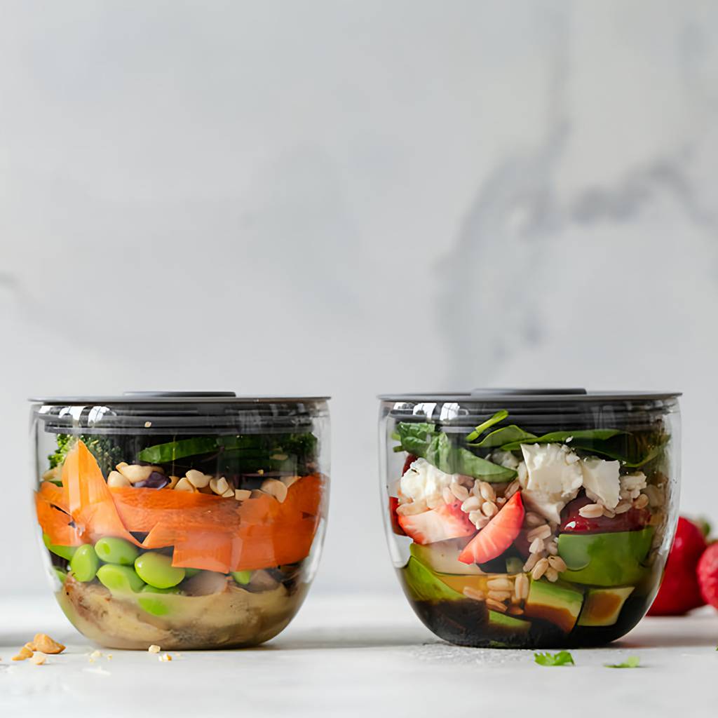 Clear containers of layered salads with greens, avocado, strawberries, grains, and vegetables.