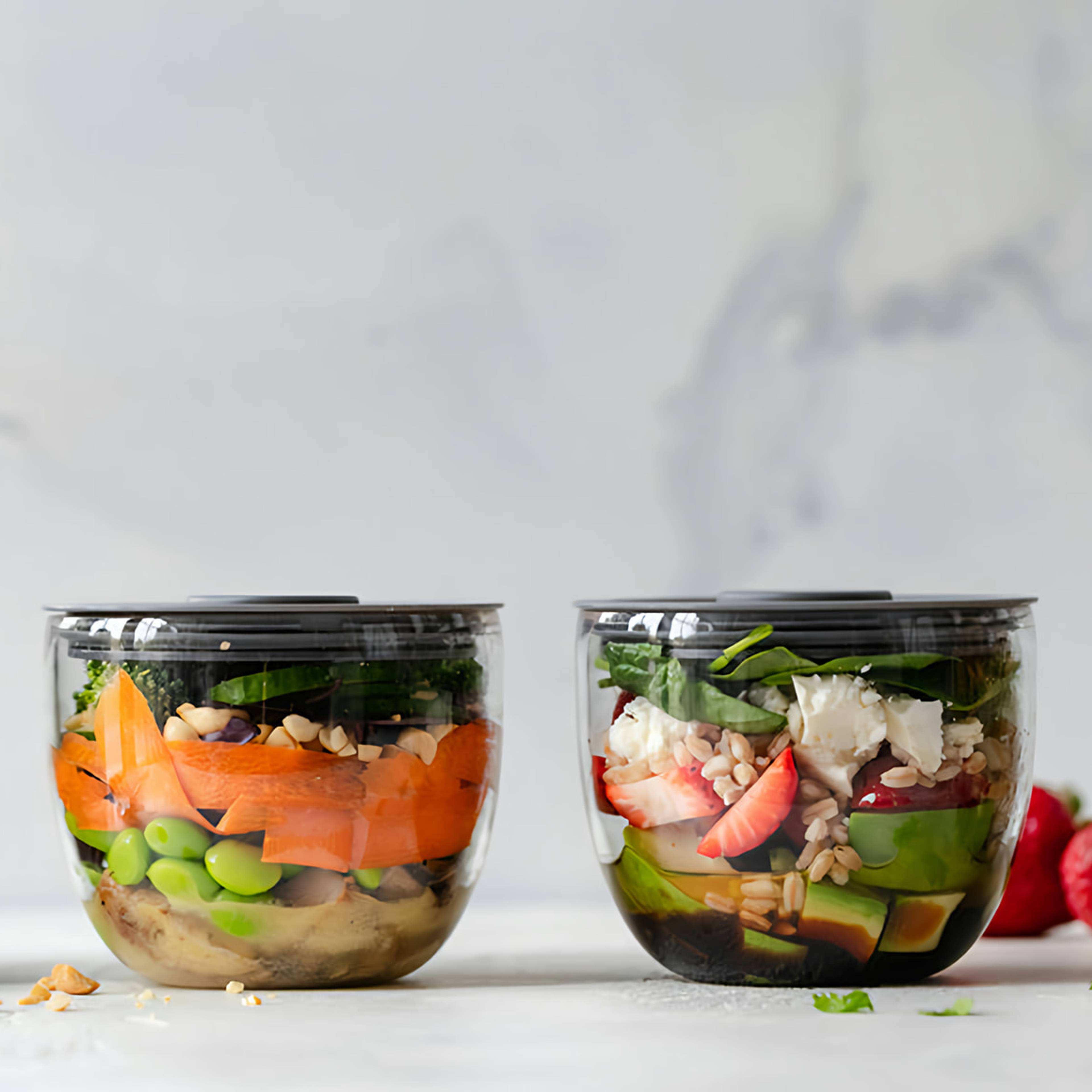 Clear containers of layered salads with greens, avocado, strawberries, grains, and vegetables.