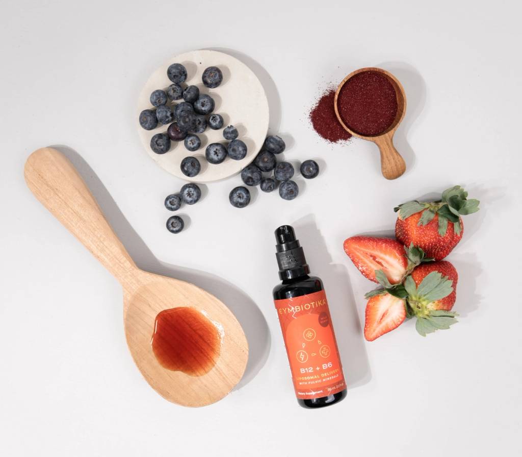 Cymbiotika Liposomal Vitamin B12 + B6 bottle with strawberries, blueberries, red powder, and a wooden spoon.
